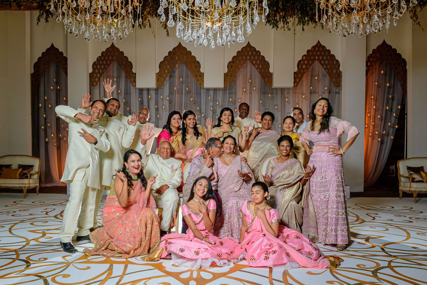 Large wedding party in pink and cream formal attire posed in elegant ballroom.