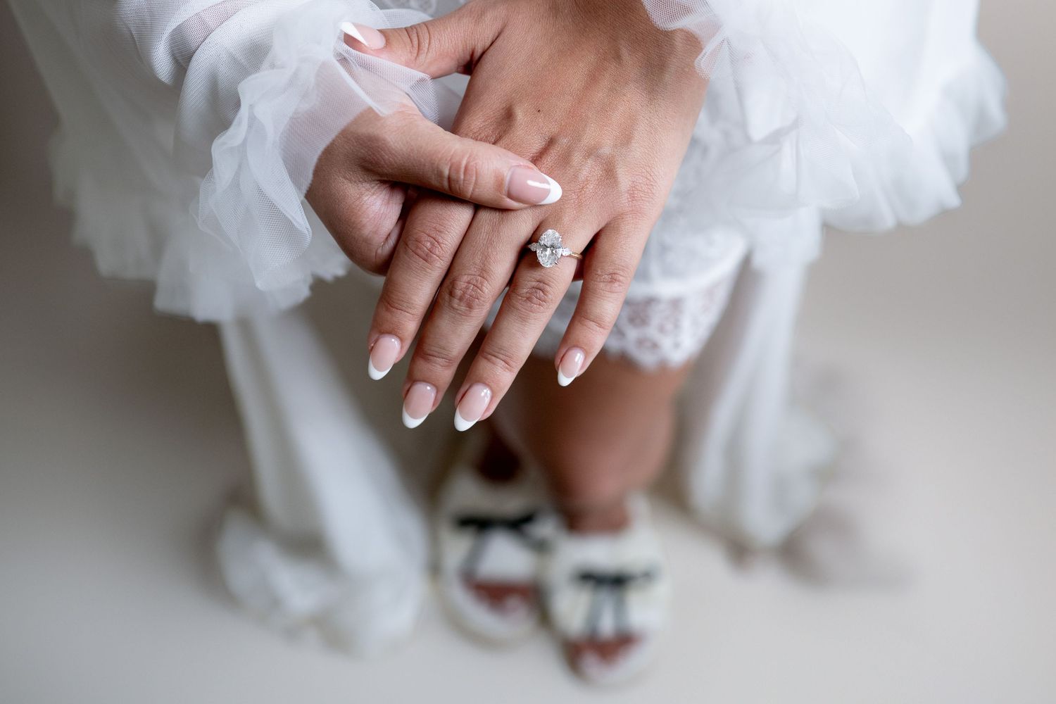 Delicate hands resting on white tulle fabric in soft lighting.