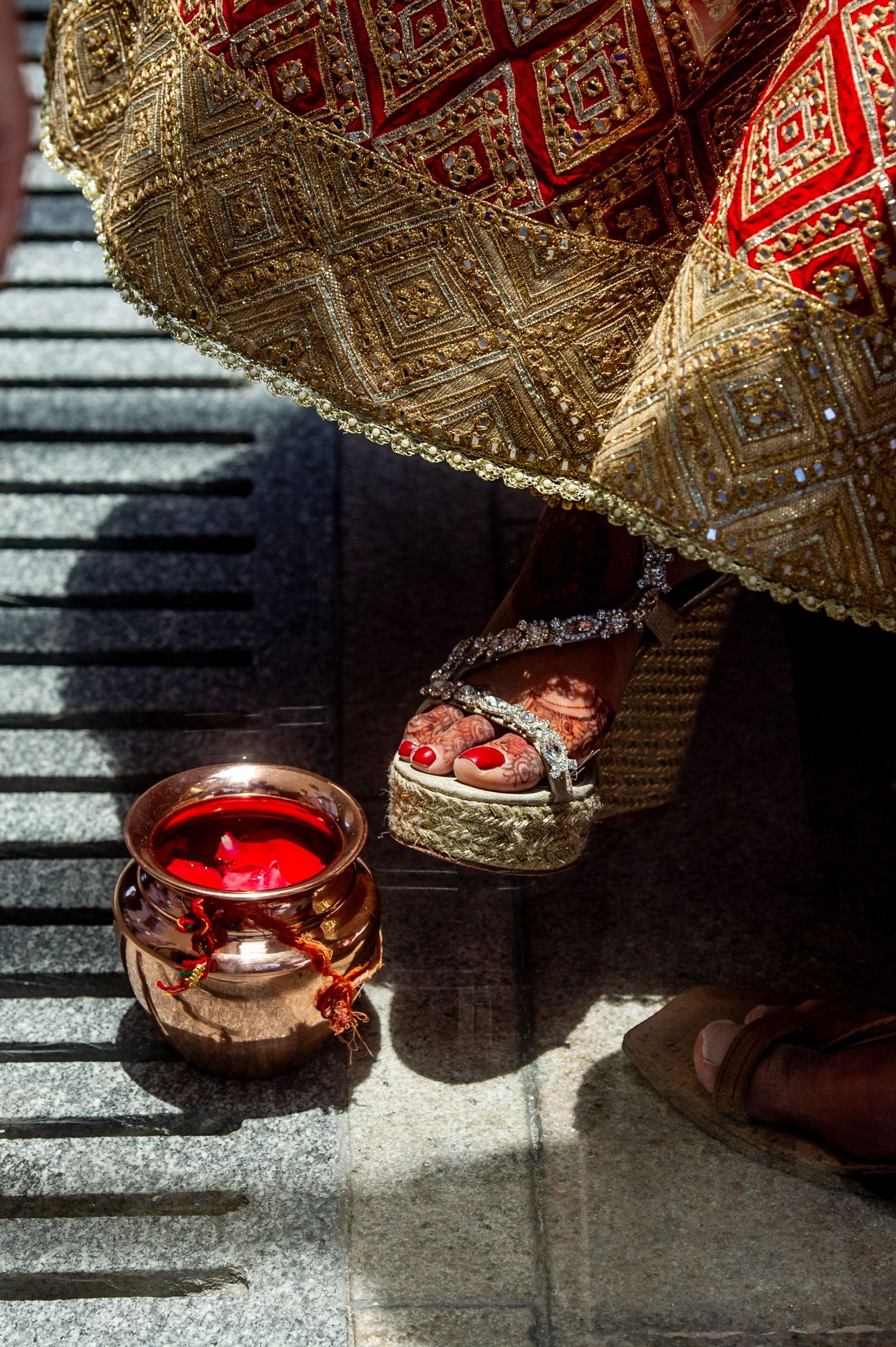Close-up of a bride's feet in ornate red sandals beside a lit oil lamp during a traditional Hindu wedding ceremony.