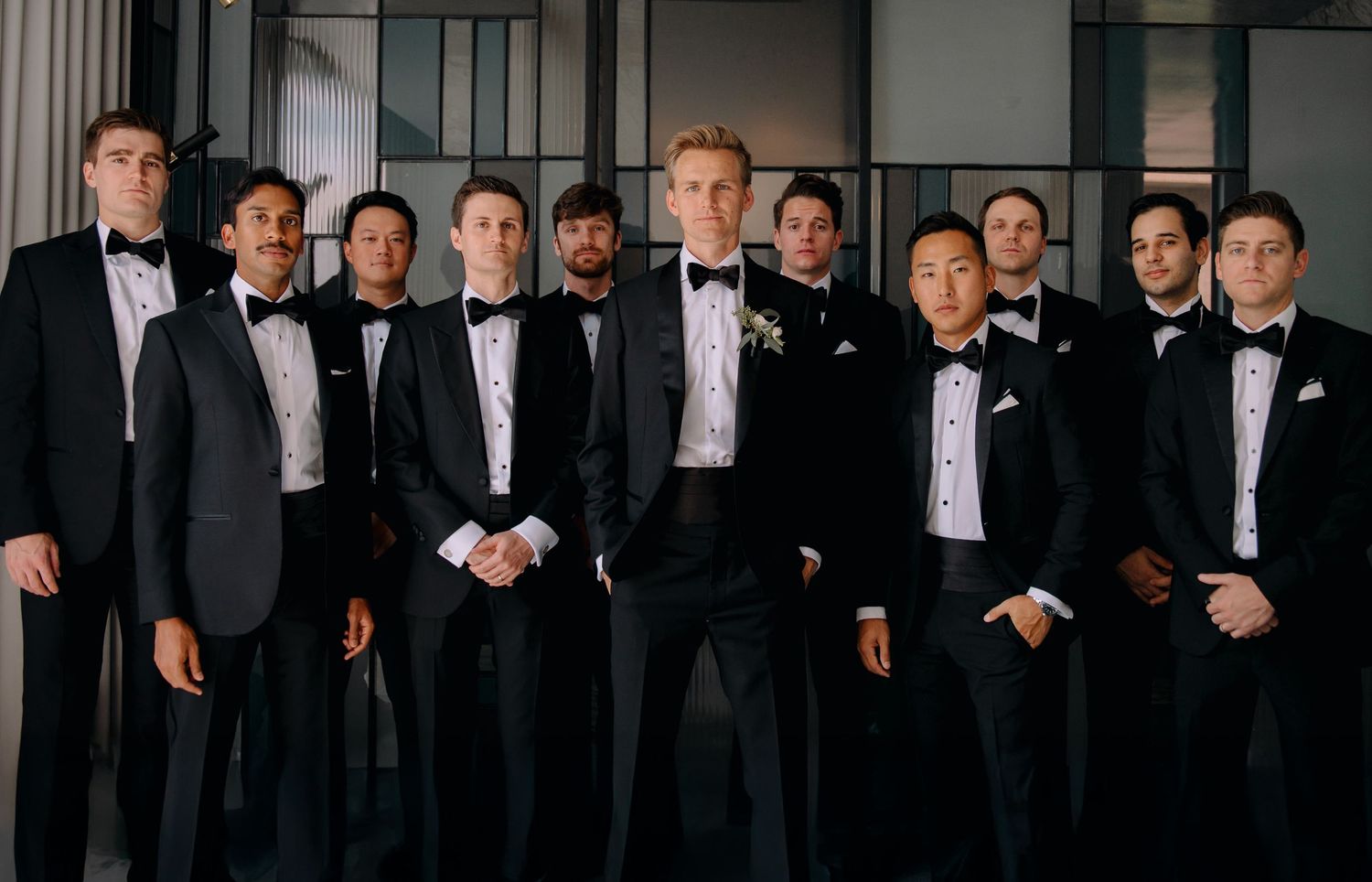 A group in formal black tuxedos and bow ties stand together for an elegant wedding party portrait.