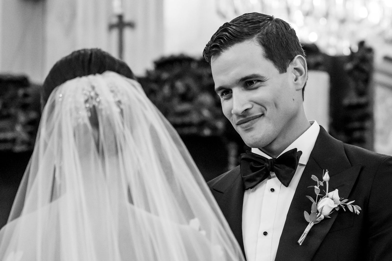 Groom smiling at veiled bride during wedding ceremony in church.