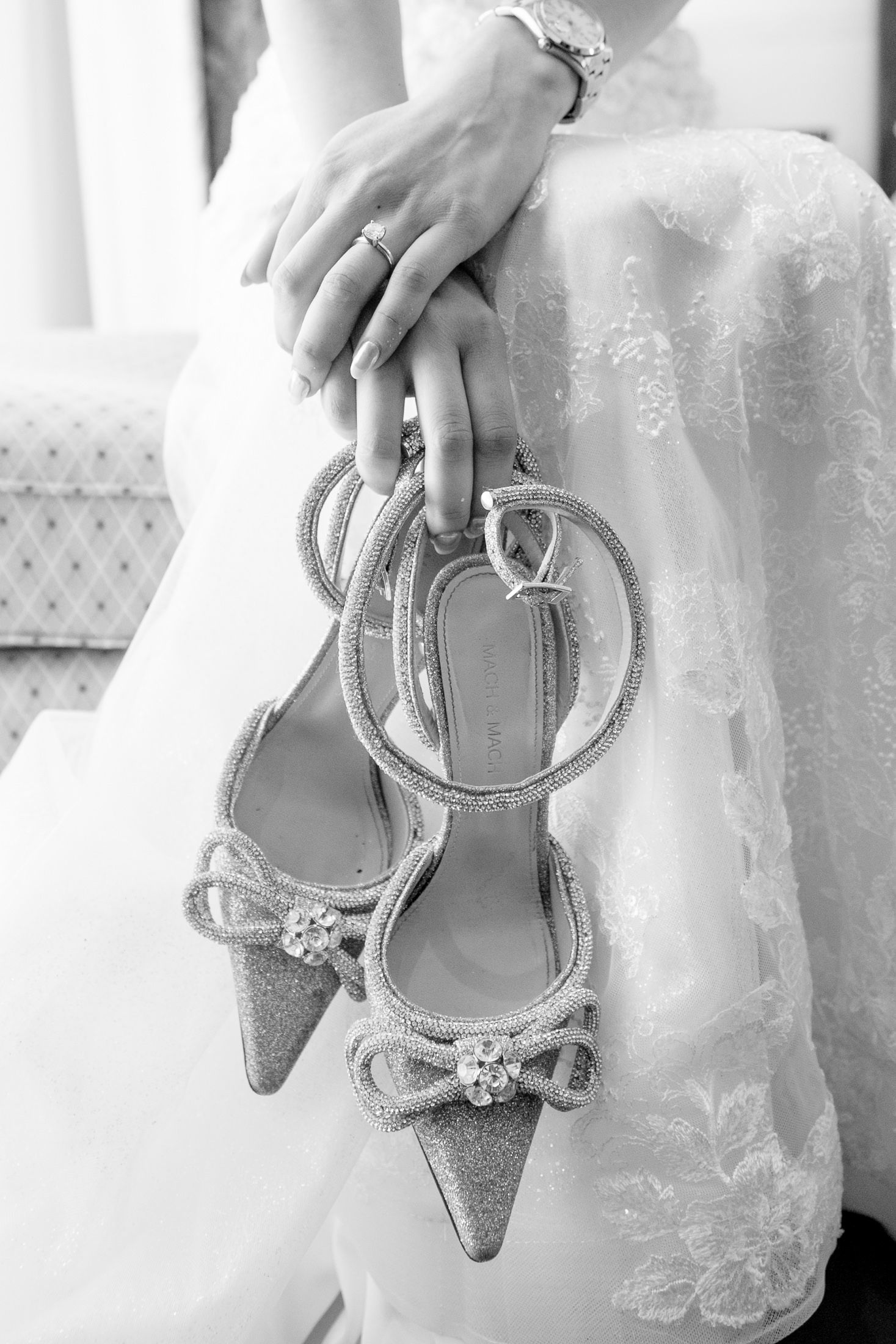 Sparkling silver bridal shoes held against white lace wedding dress.