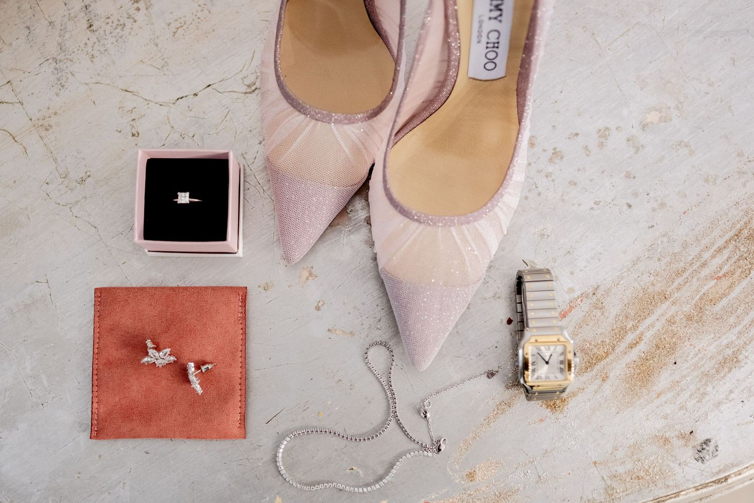 Blush pink bridal shoes with jewelry and accessories on marble surface.