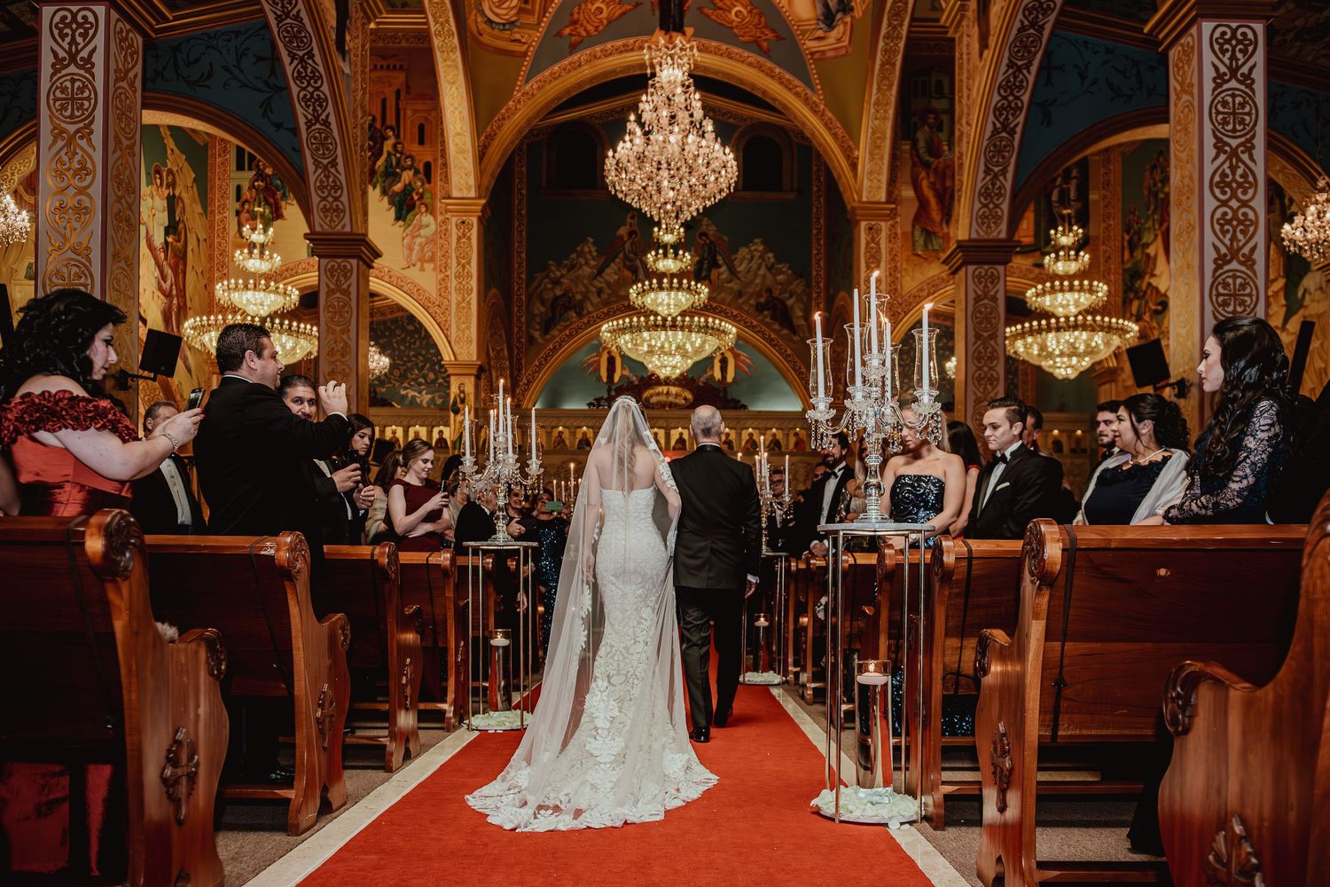 Elegant ballroom wedding reception with ornate chandeliers and decorative details in warm lighting.