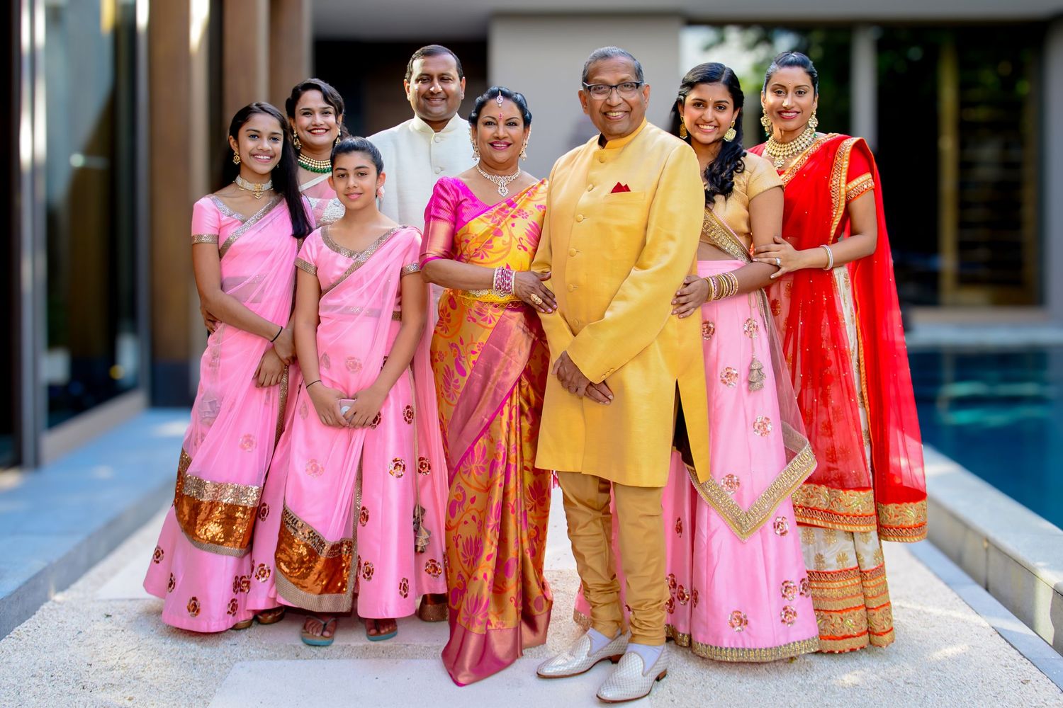 Indian family in traditional attire, women in pink and red sarees, men in kurta, posing together at a festive celebration.