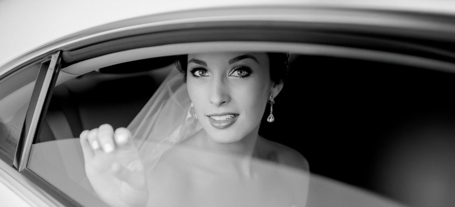 Elegant black and white portrait of a bride smiling in a car window with classic Hollywood glamour styling.