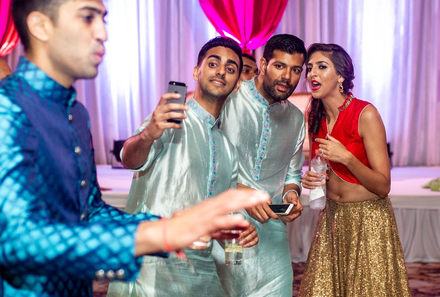 Group of friends in colorful Indian attire taking a selfie at a festive celebration event.