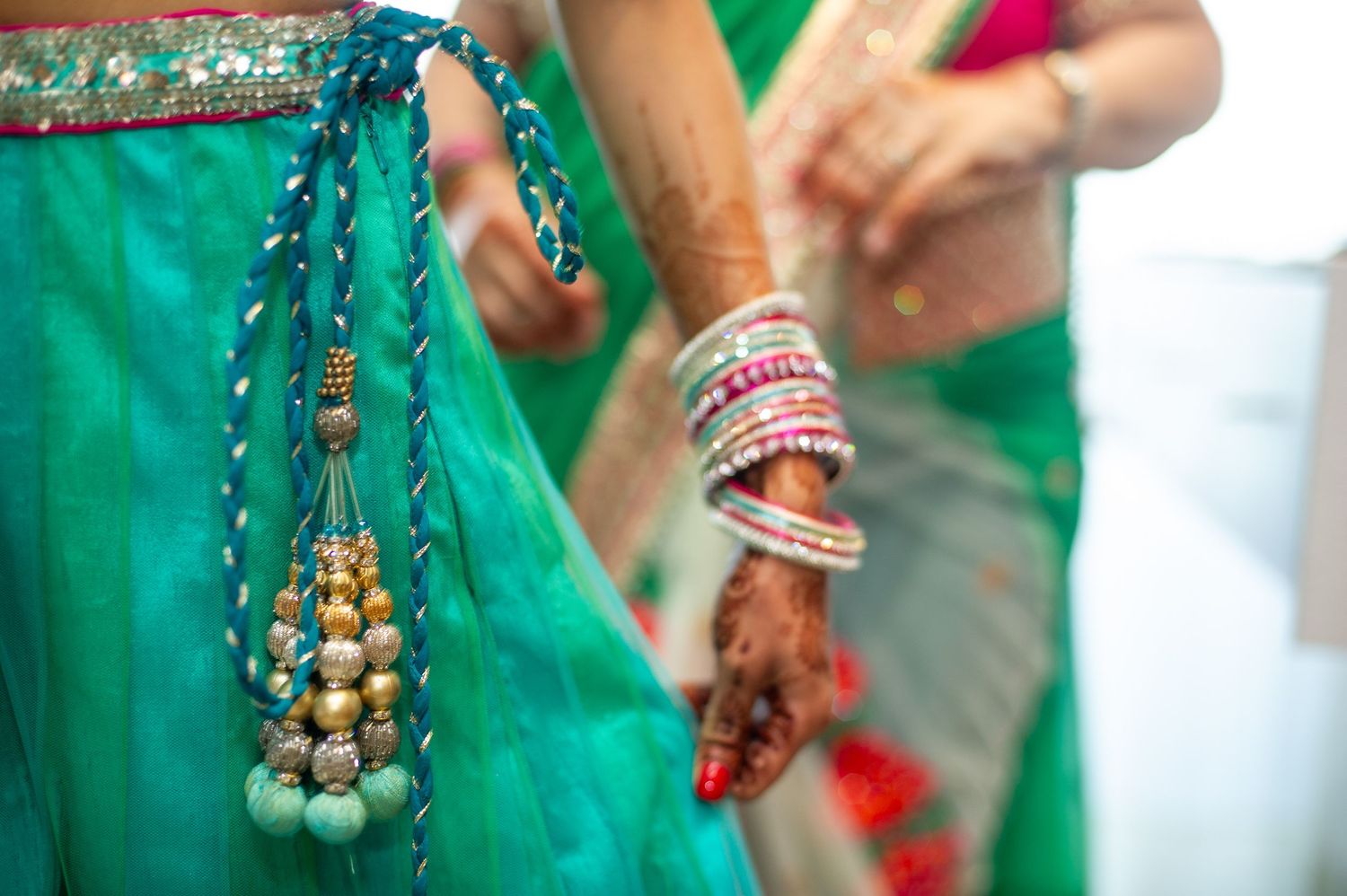 Close-up of Indian bride in green saree with decorative tassel and colorful bangles with mehndi henna on hands.