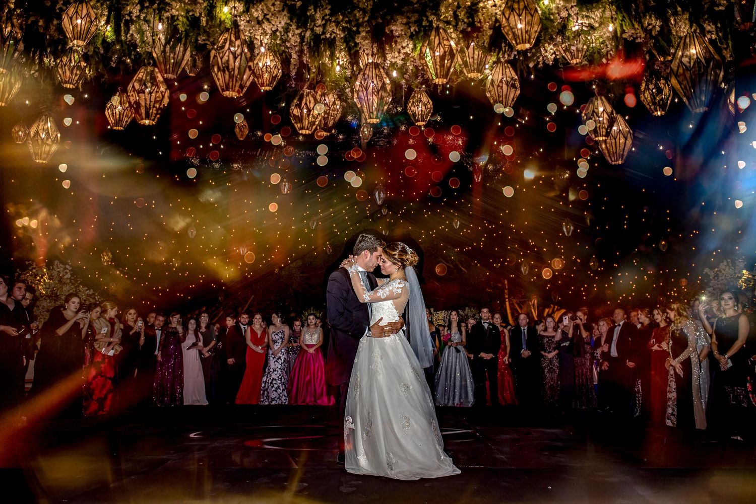 Couple dancing under twinkling lights and chandeliers at a luxurious evening wedding reception.