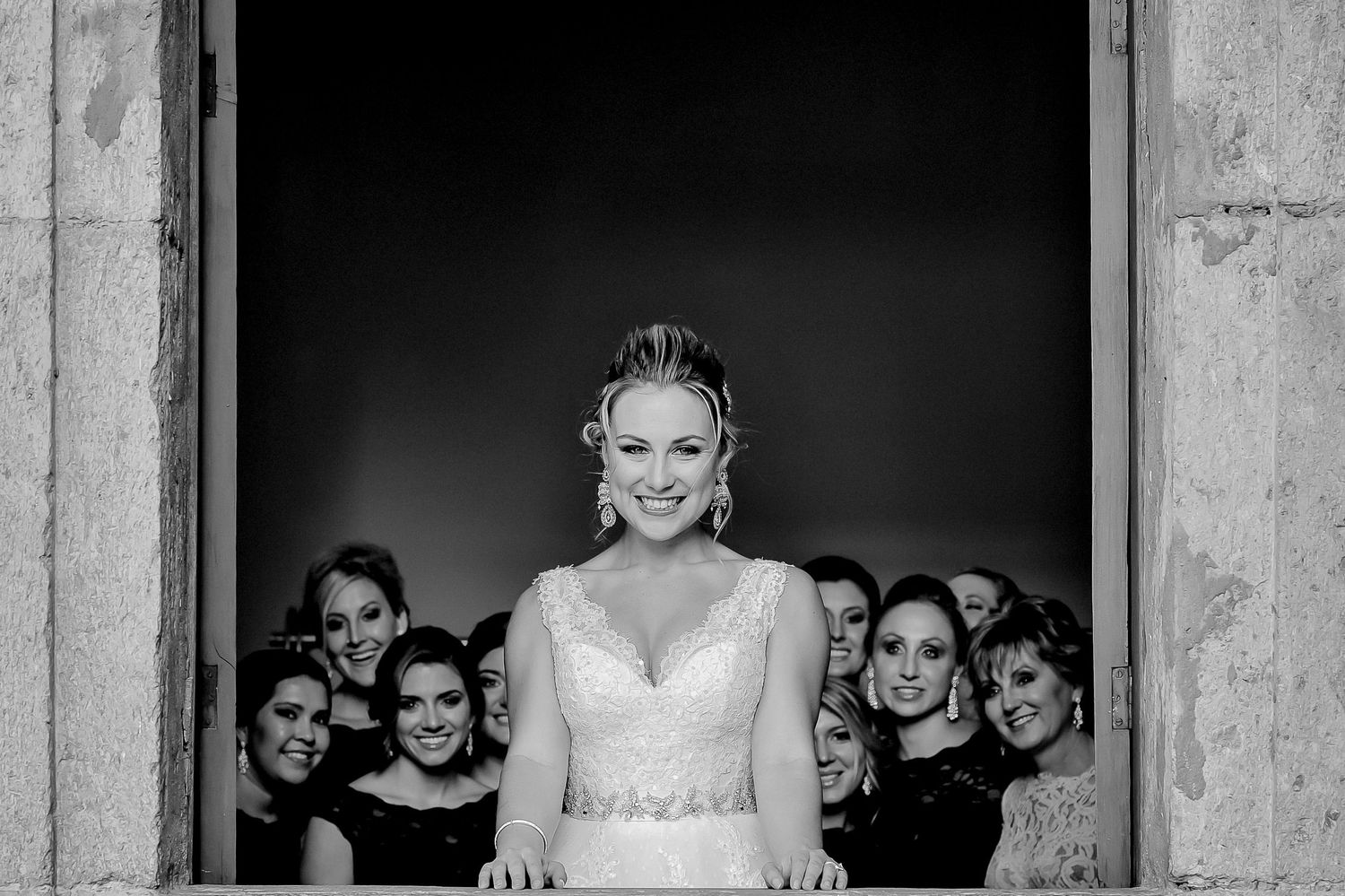 Black and white wedding photo showing a bride surrounded by bridesmaids in a dramatic doorway.