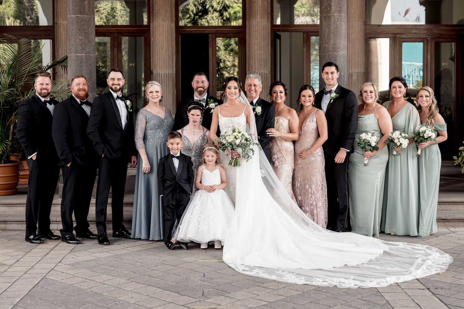 Wedding party poses under covered walkway with classic architectural columns.
