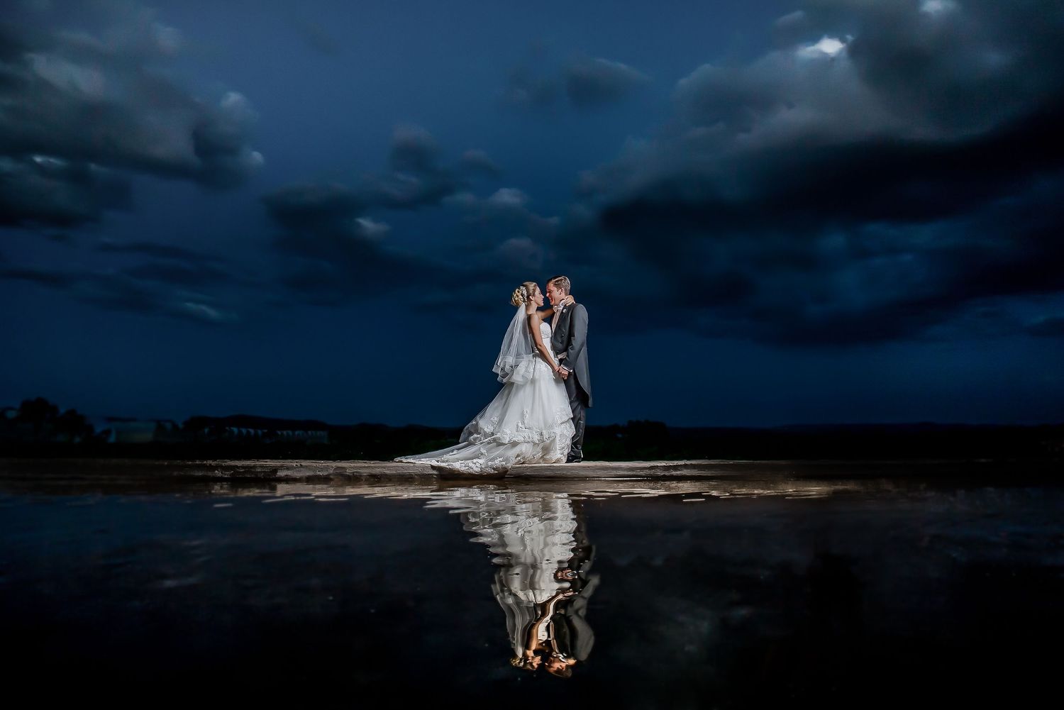 Dramatic wedding photos against stormy dark blue sky at sunset.