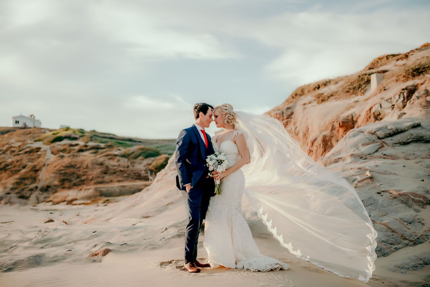 Dramatic wedding photography on rocky cliffs with flowing veil catching the wind.