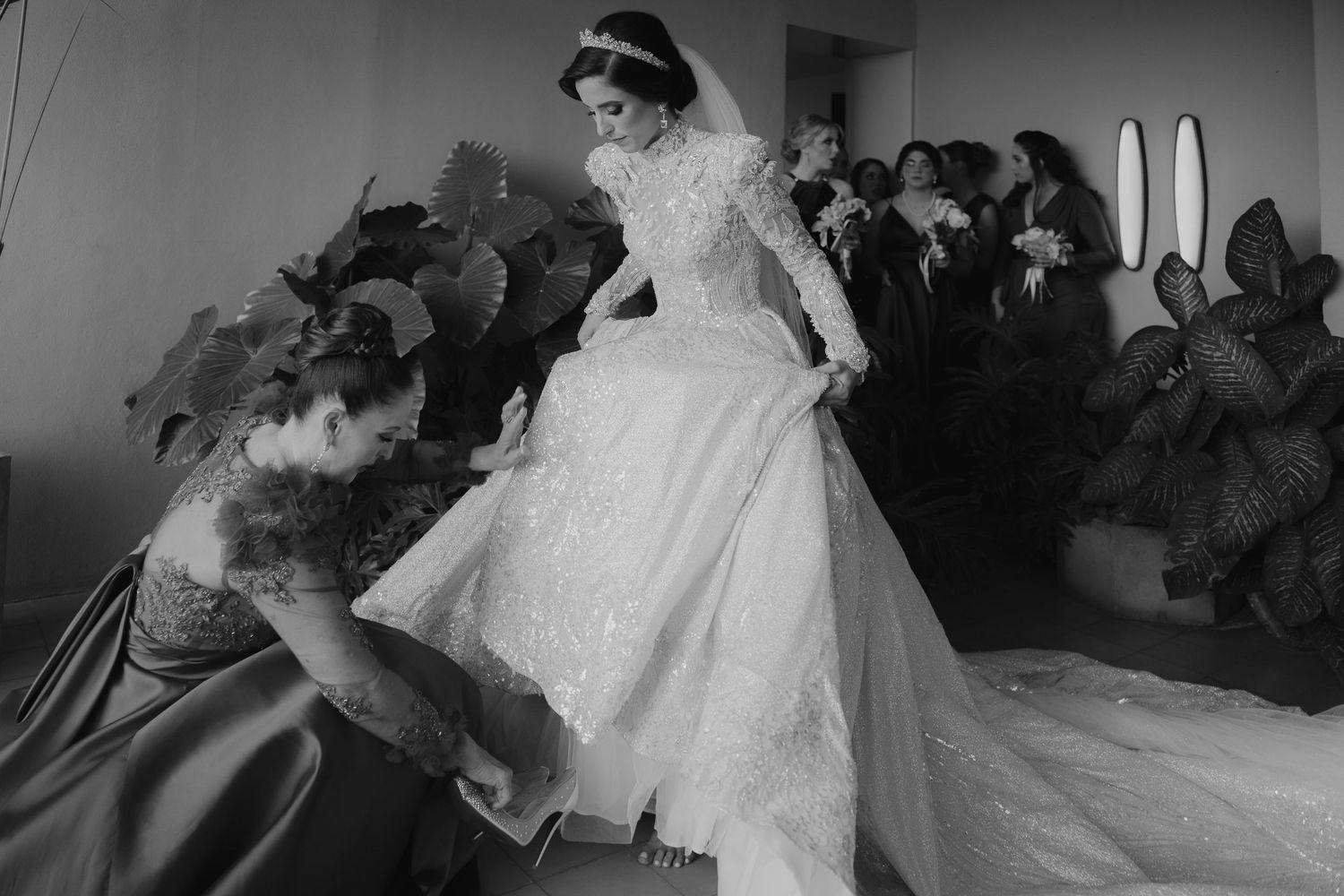 Black and white photo of a bride in a ballgown being assisted by attendants before her wedding ceremony.