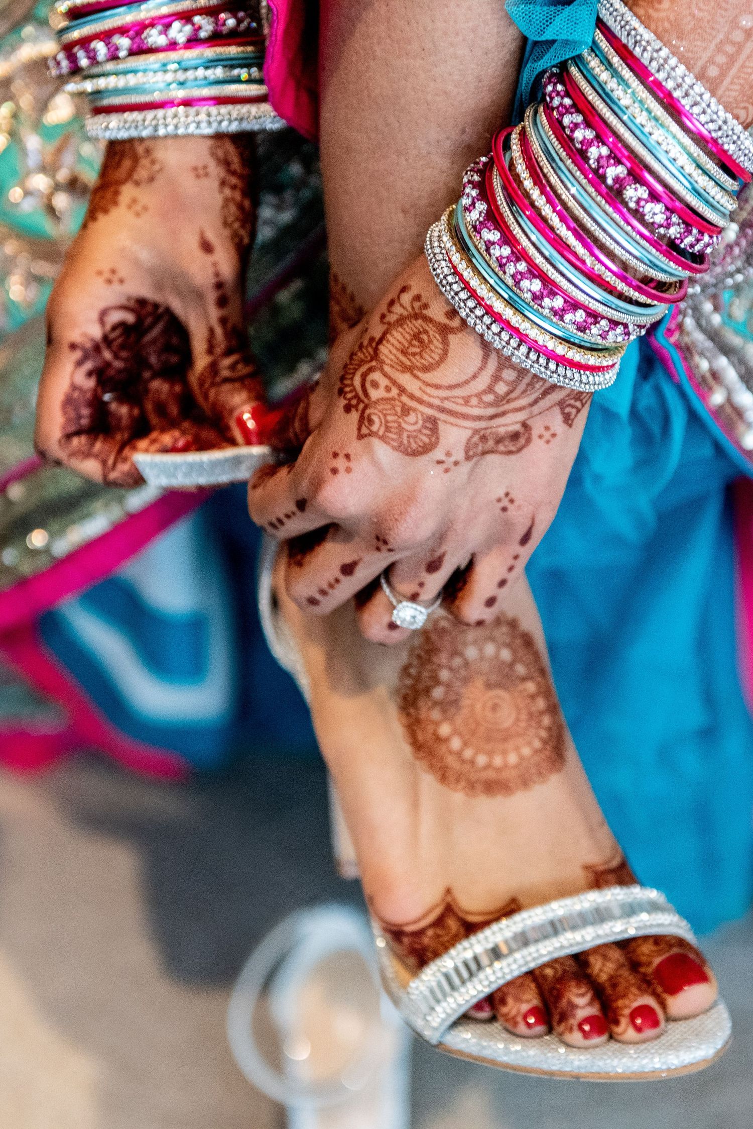 Bride's hands adorned with intricate henna mehndi designs, colorful bangles, and a diamond ring at an Indian wedding.