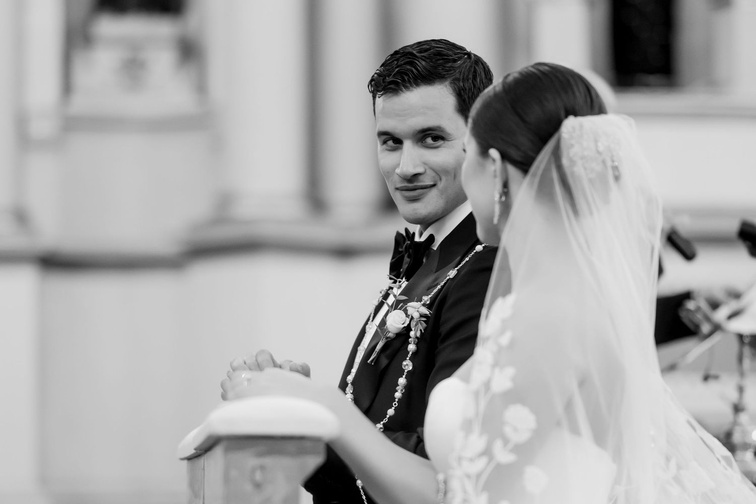 Groom smiling at bride during outdoor wedding ceremony in black and white.
