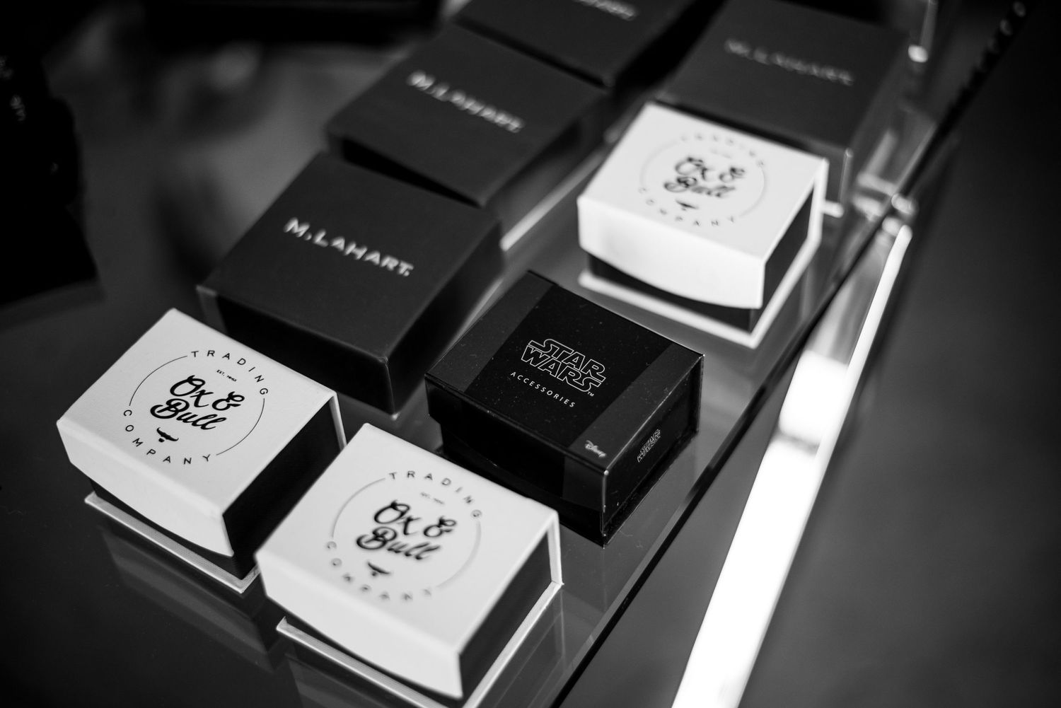 Black and white photo of M.Lamare and Ch&Smile branded jewelry gift boxes displayed on a reflective surface.