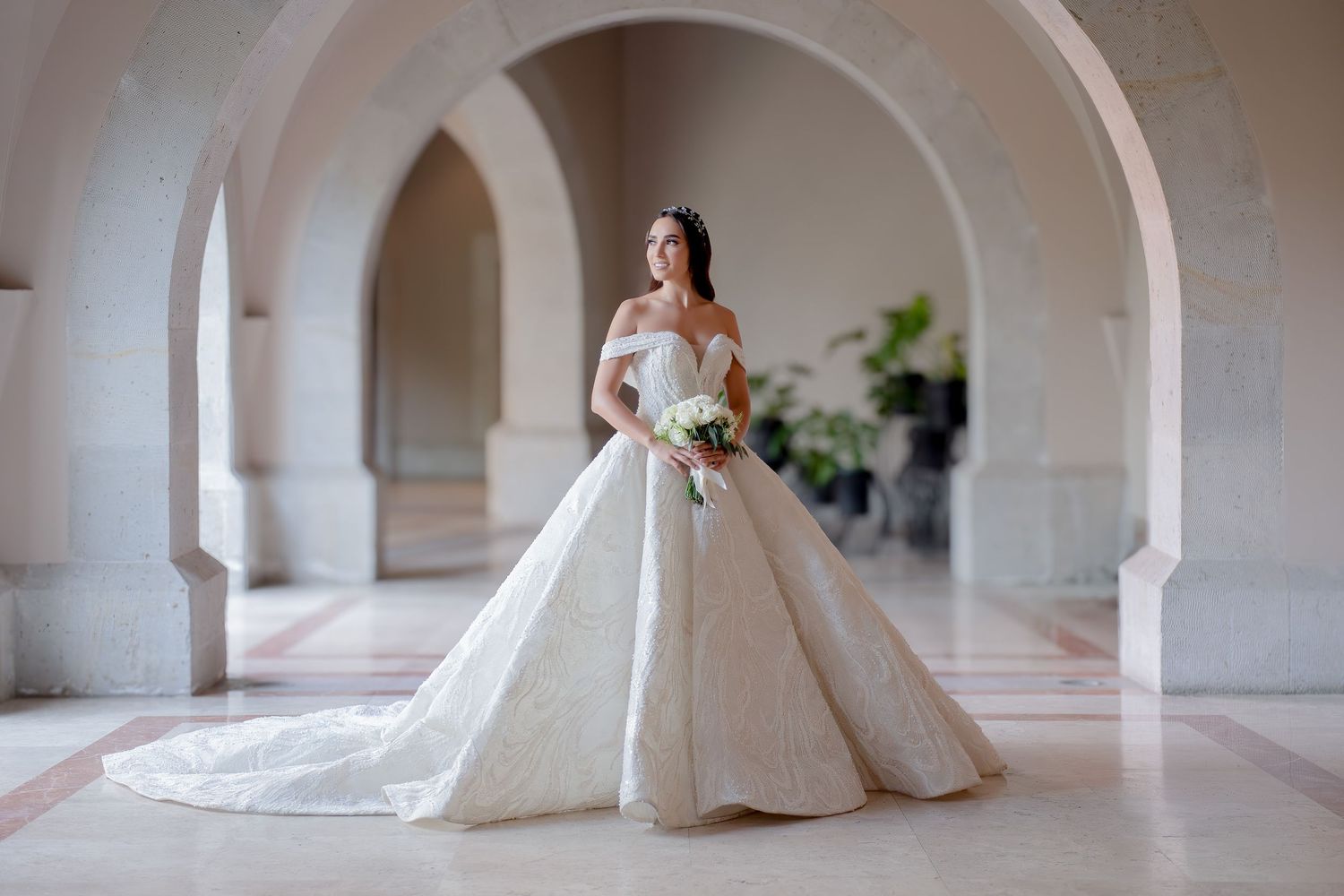 Majestic ball gown wedding dress photographed under arched colonnade with trailing veil.