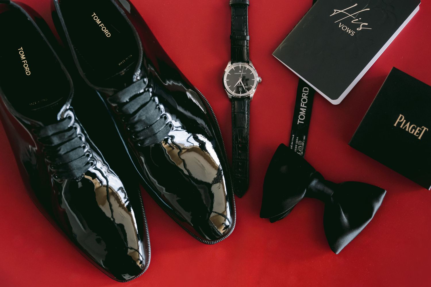 Collection of formal black dress shoes and accessories arranged on red background.