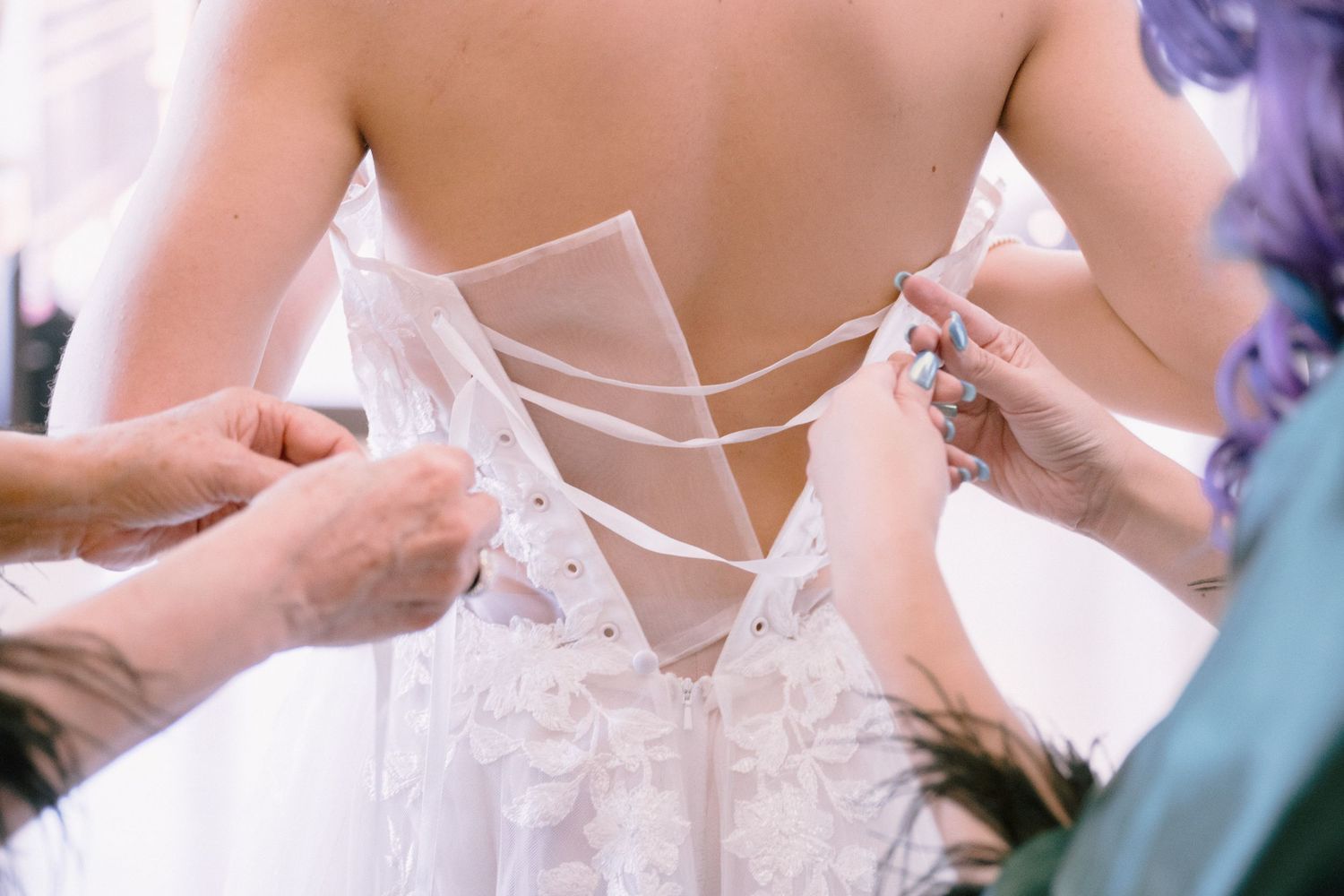 Detail shot of corset back wedding dress being laced up with delicate ribbons.