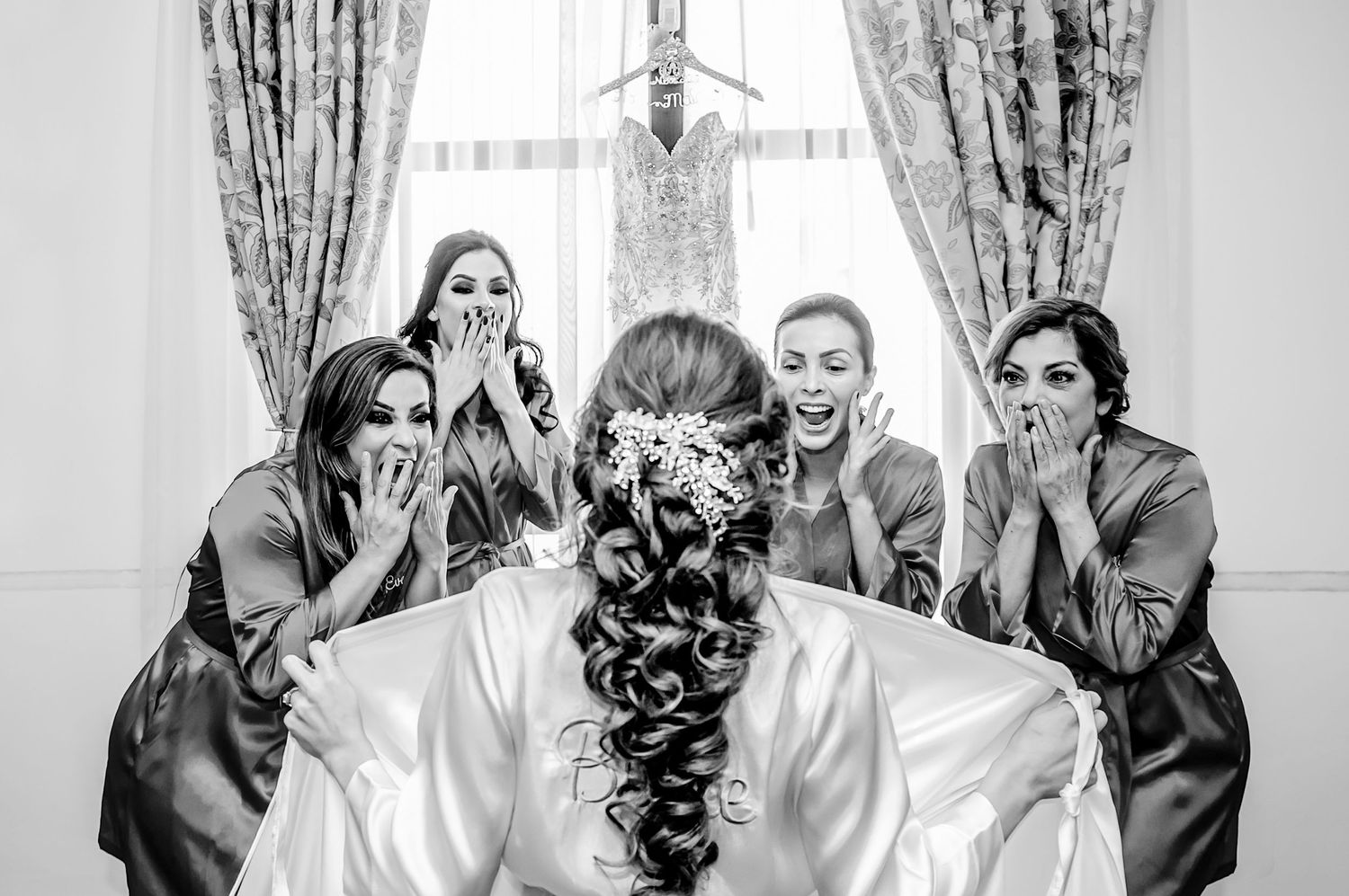 Black and white photo showing excited reactions during a wedding preparation moment.