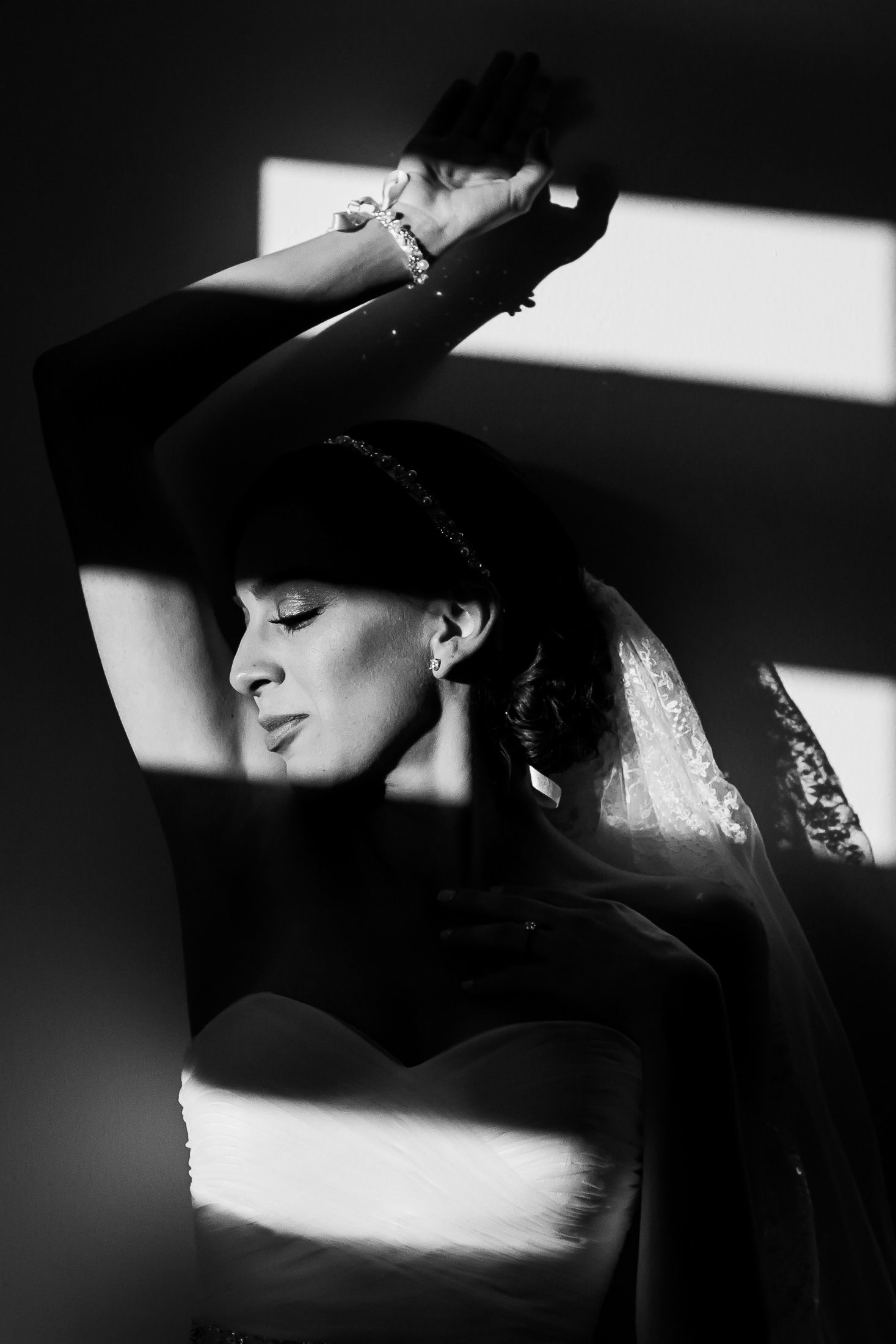 Dramatic black and white photo of a bride in veil with raised arms creating artistic shadows.