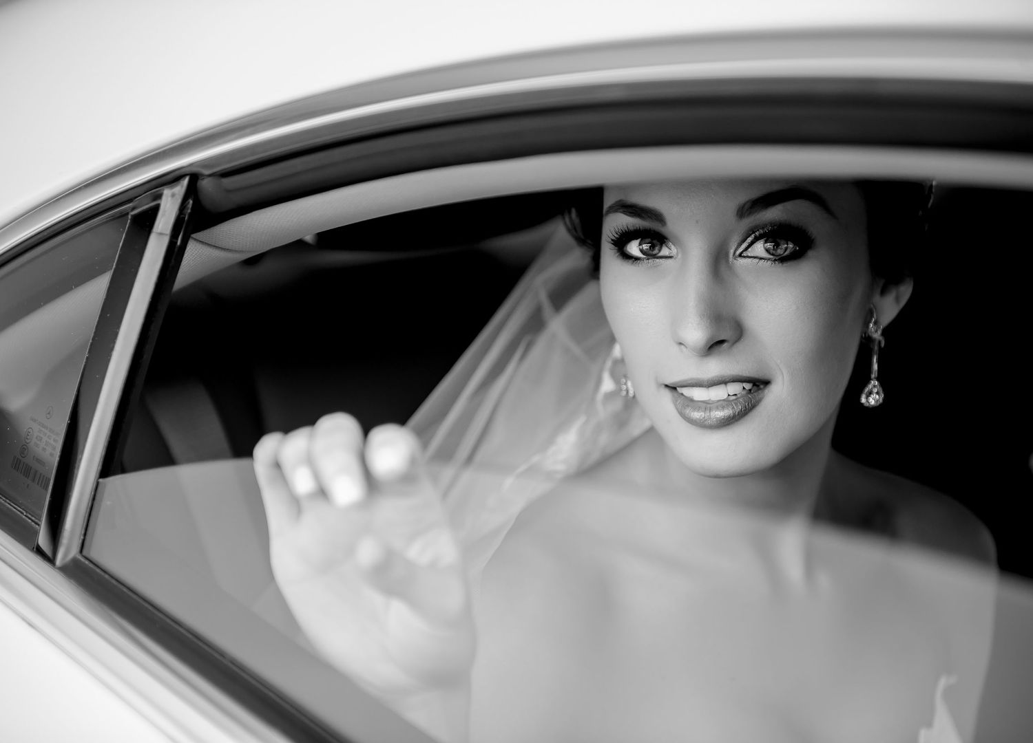 A classic black and white portrait of a bride smiling from inside a vintage car.