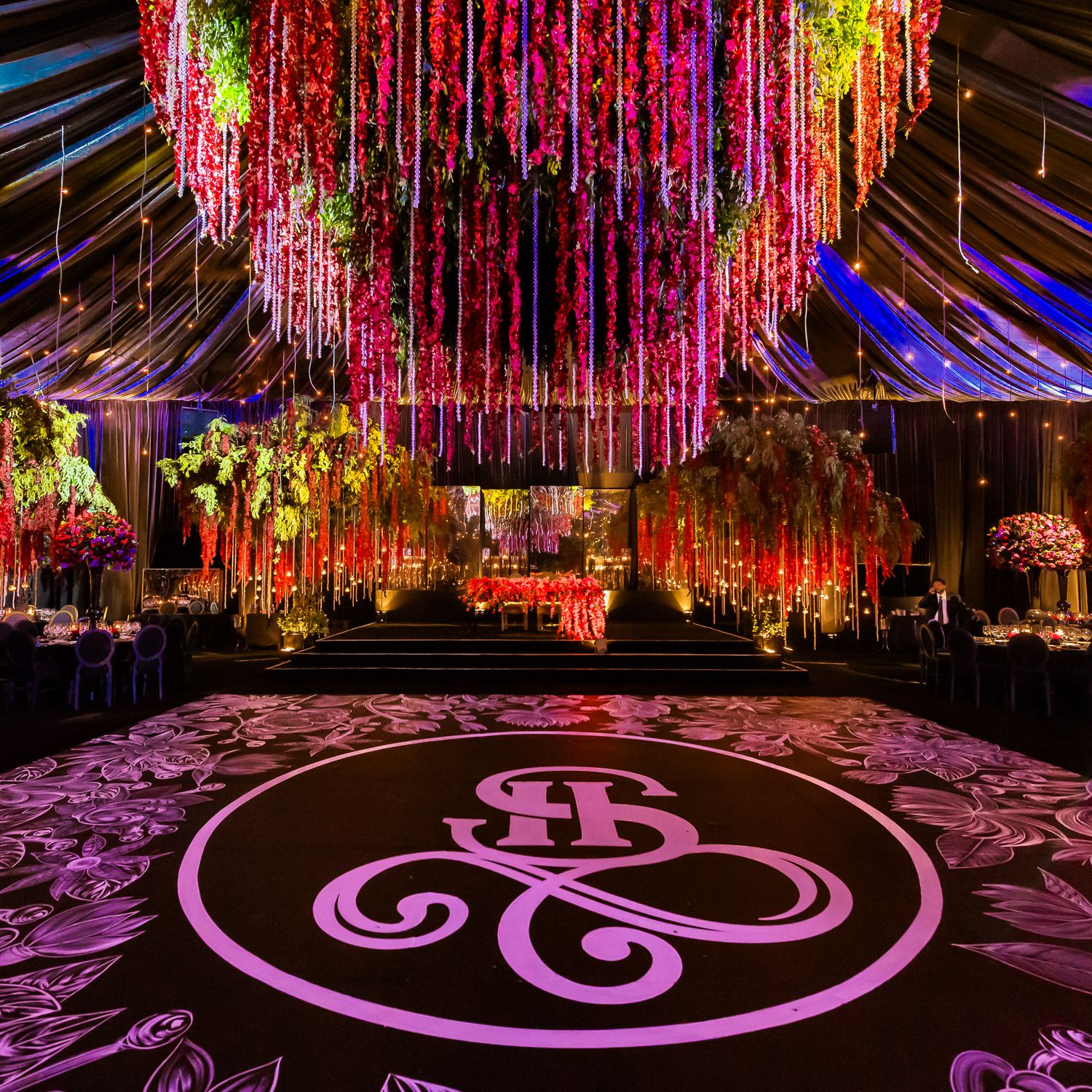 Purple-lit dance floor with illuminated monogram design under dramatic hanging floral installations.