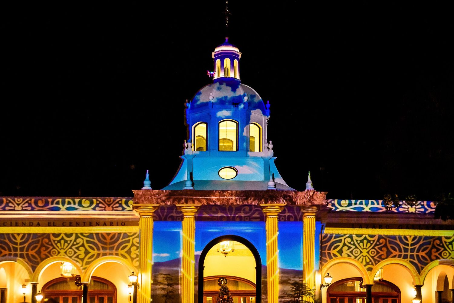 Colorful light projections illuminate a historic building with a blue dome at night.