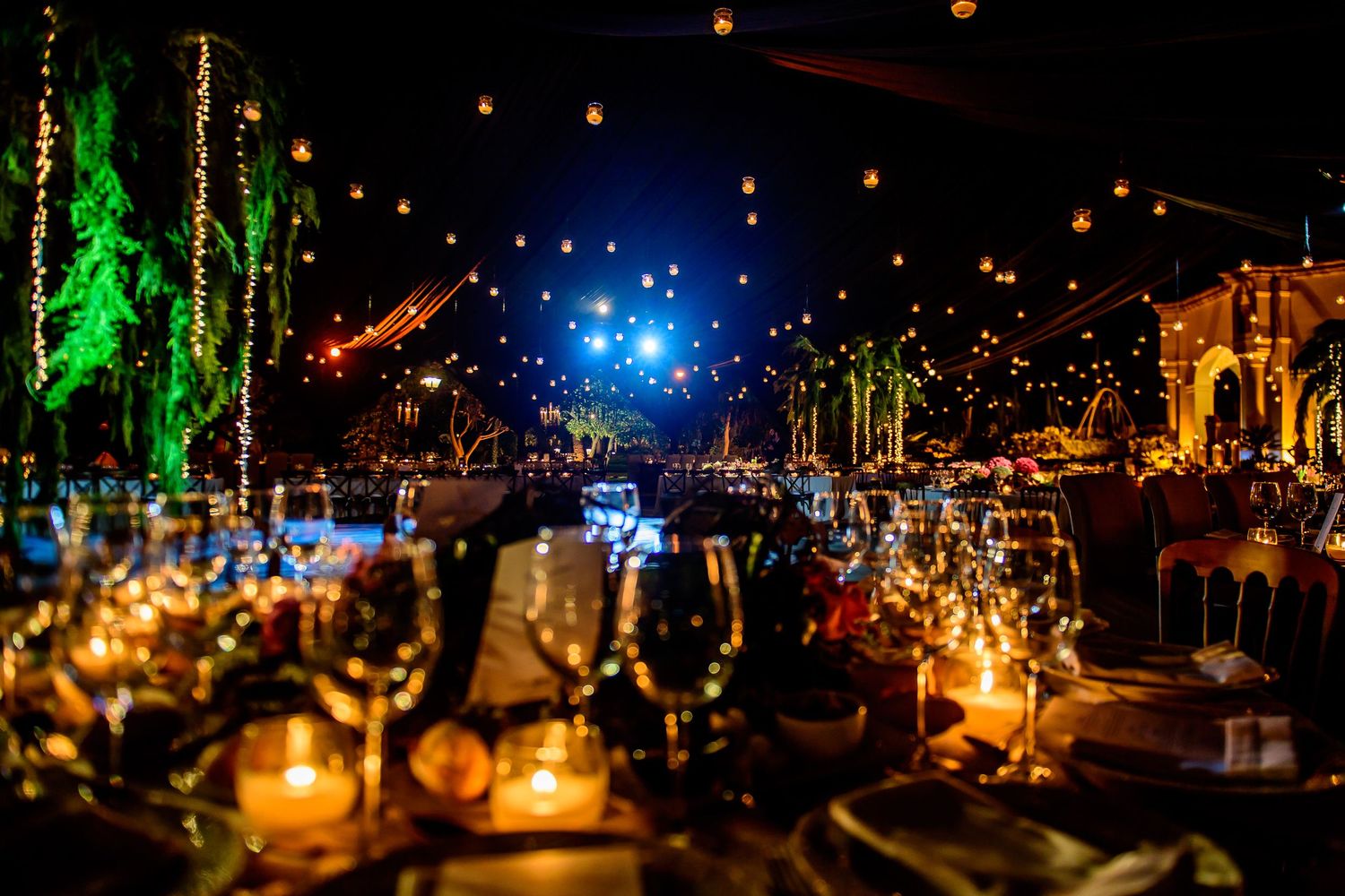 Romantic candlelit table settings under twinkling lights and greenery at an evening wedding reception.