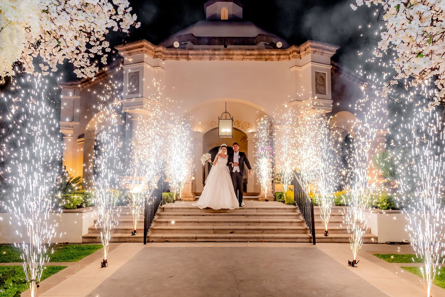 Grand wedding venue entrance with sparkler fountains illuminating stone steps at night.