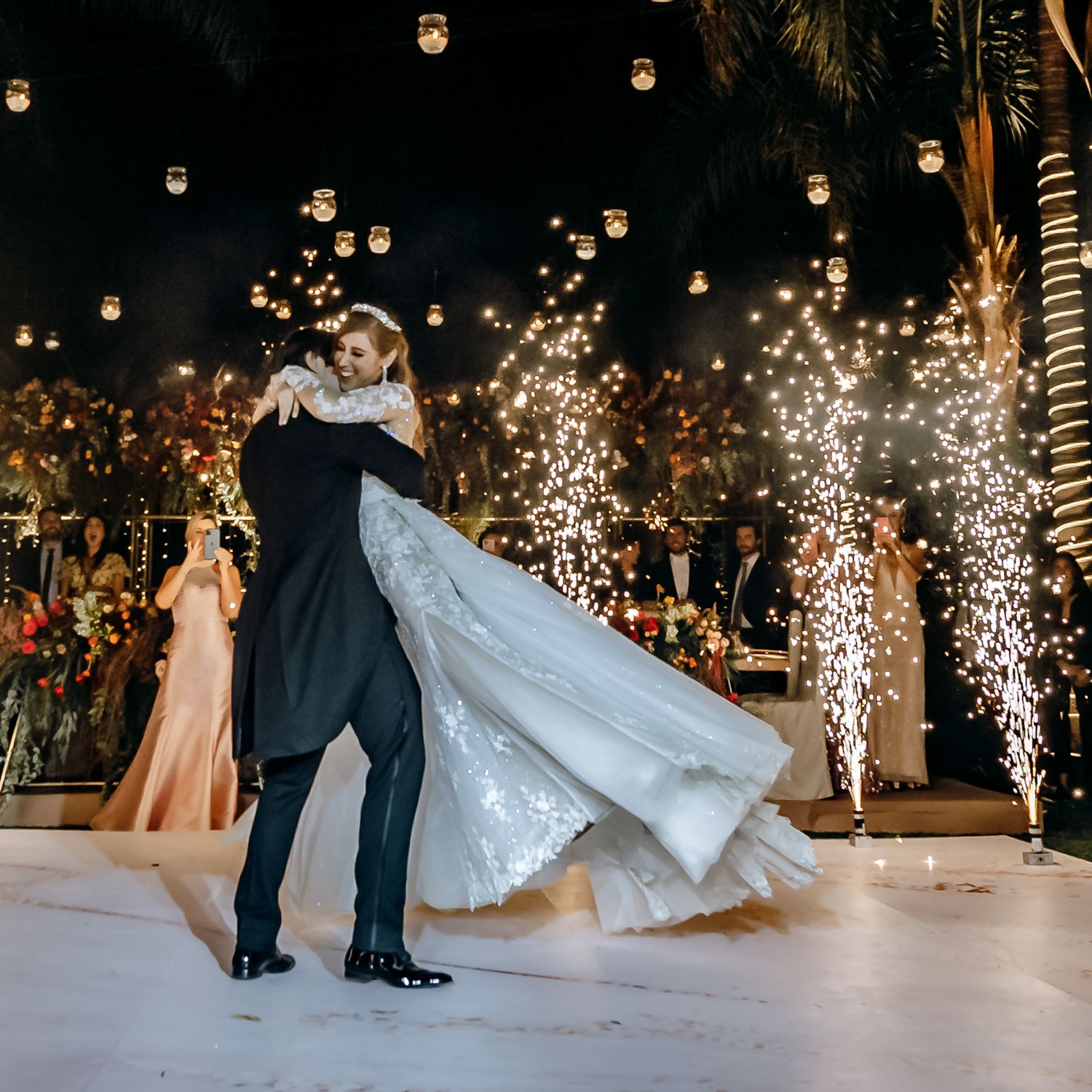 Wedding couple's first dance with dramatic sparkler effects on white dance floor.