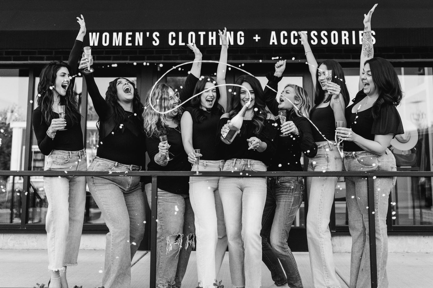 Group of women celebrating and jumping in front of clothing store sign.