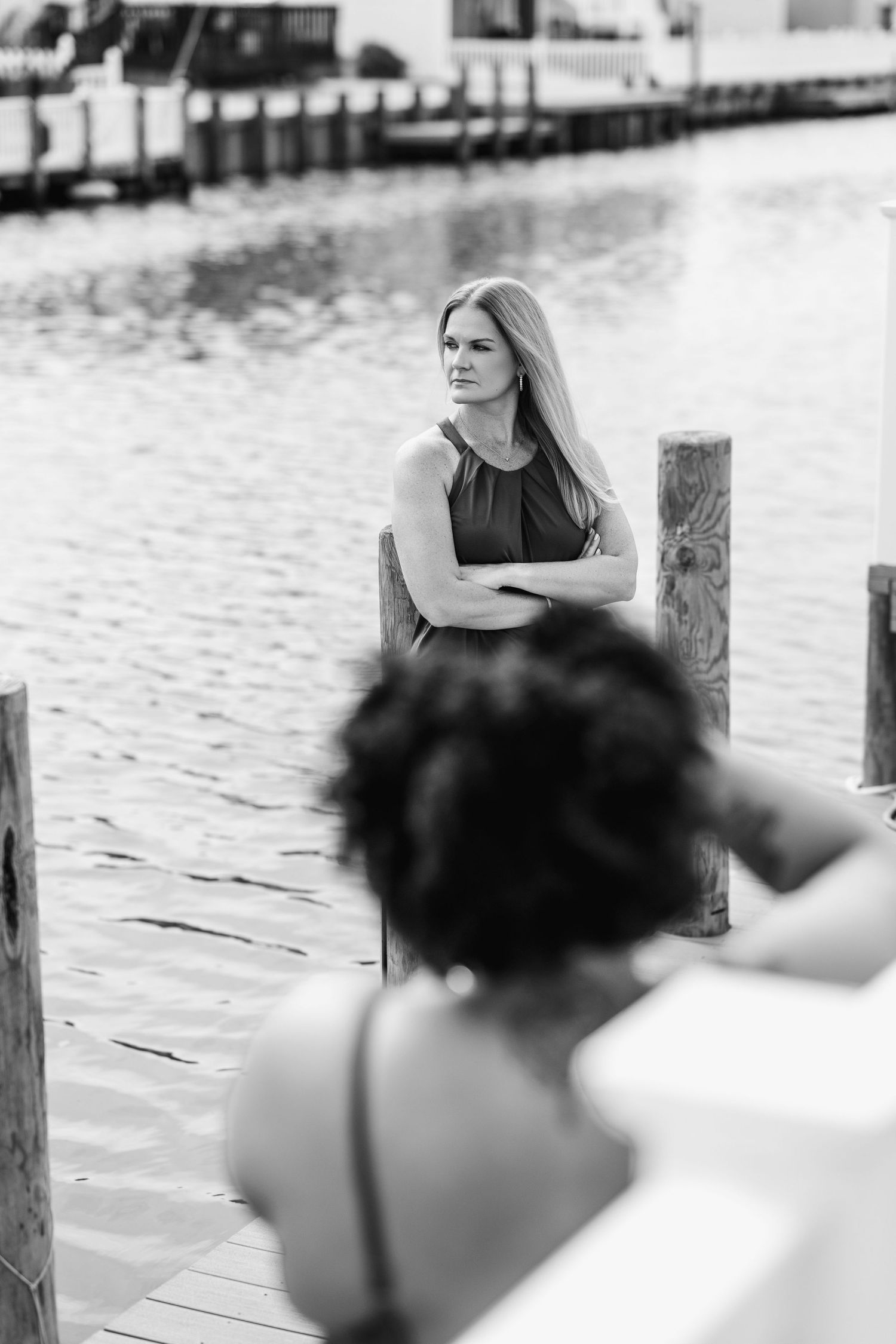 Black and white photo of woman posing on a wooden dock by the water.