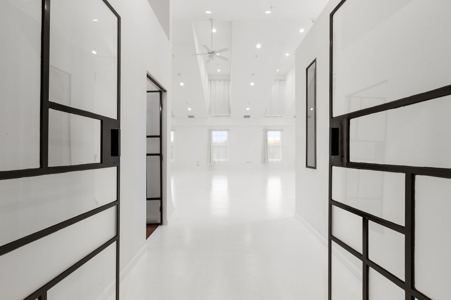 Modern white hallway with black-framed glass doors, recessed lighting, and glossy white floors in a minimalist interior.