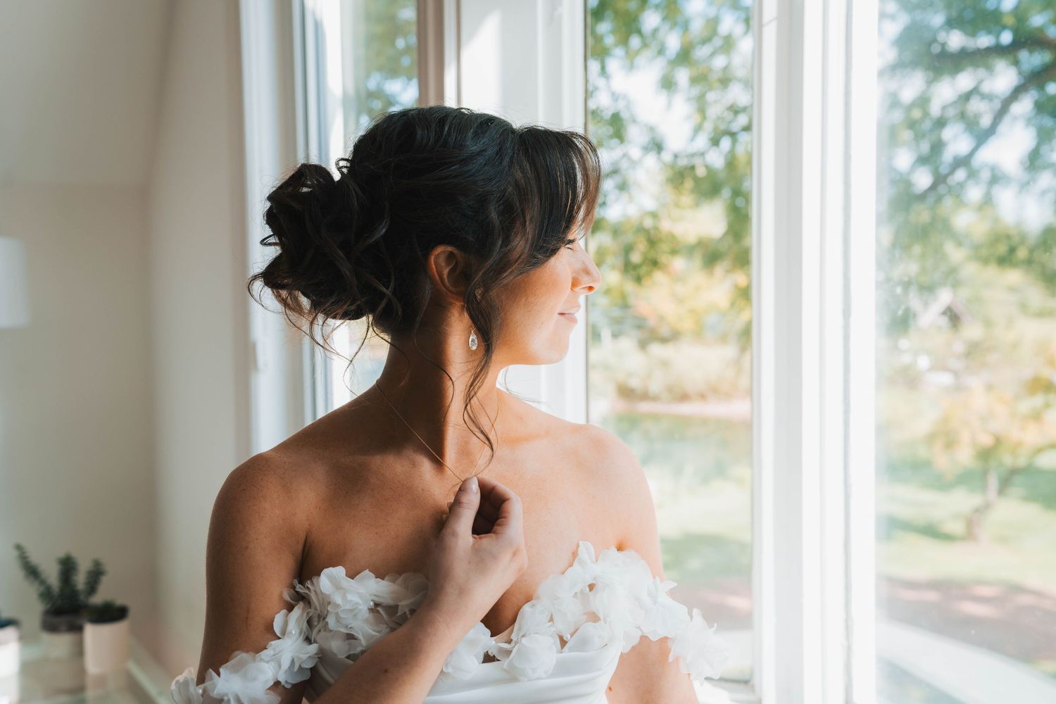 A wedding photographer captures intimate moments of a bride getting ready by a sunlit window.
