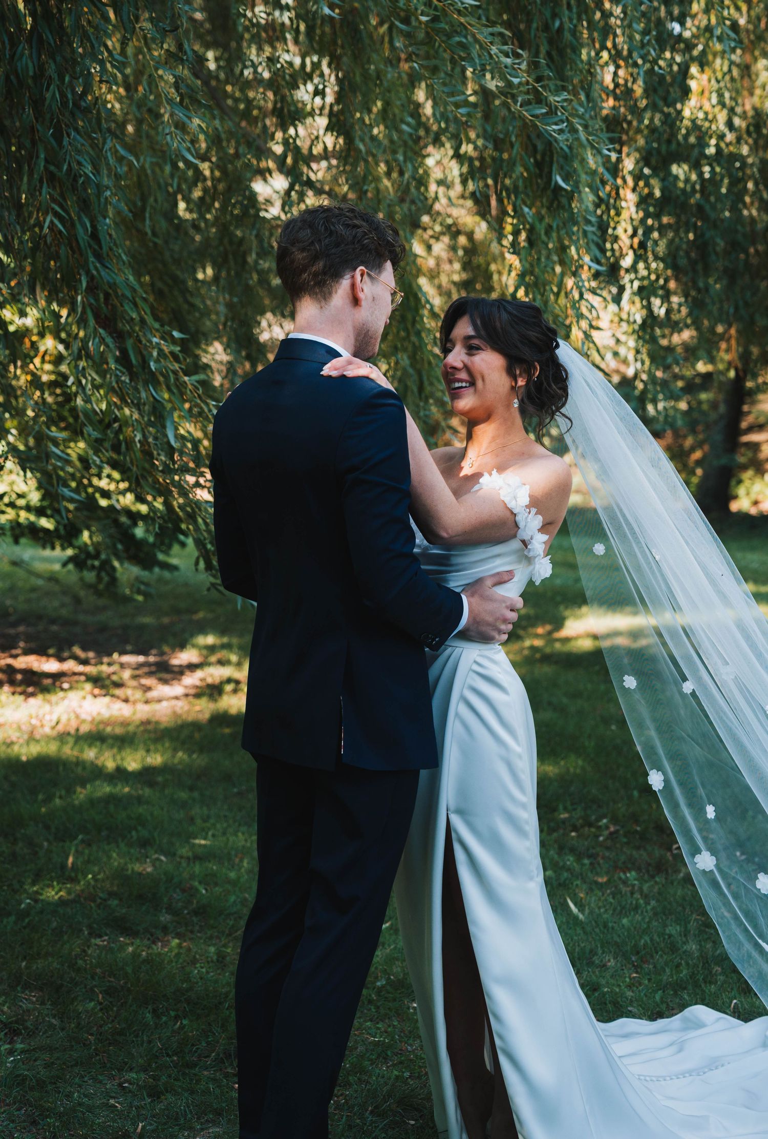 A couple shares a romantic moment under willow trees during their outdoor wedding ceremony.