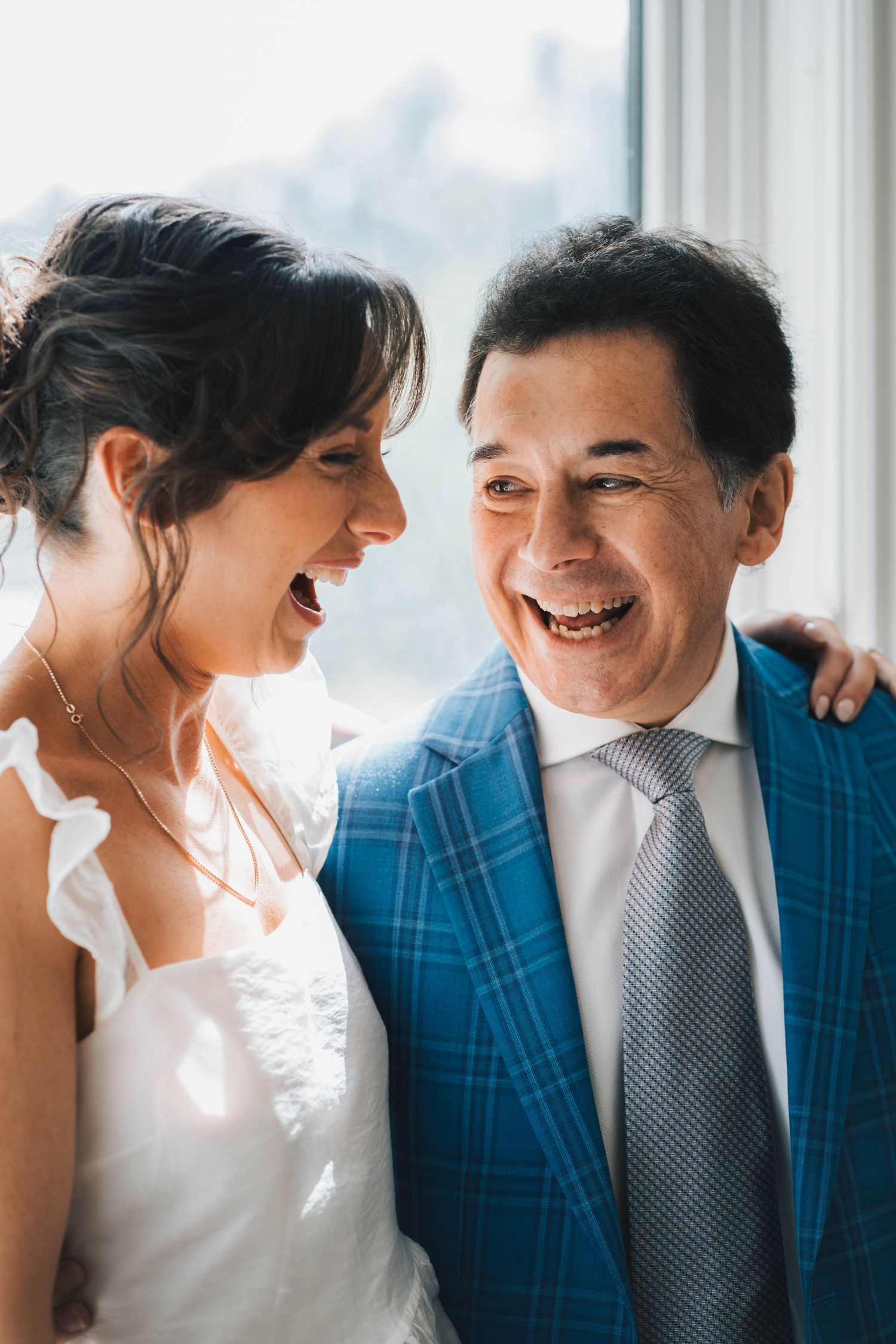 A couple in wedding attire share joyful candid moments together in a bright sunlit setting.