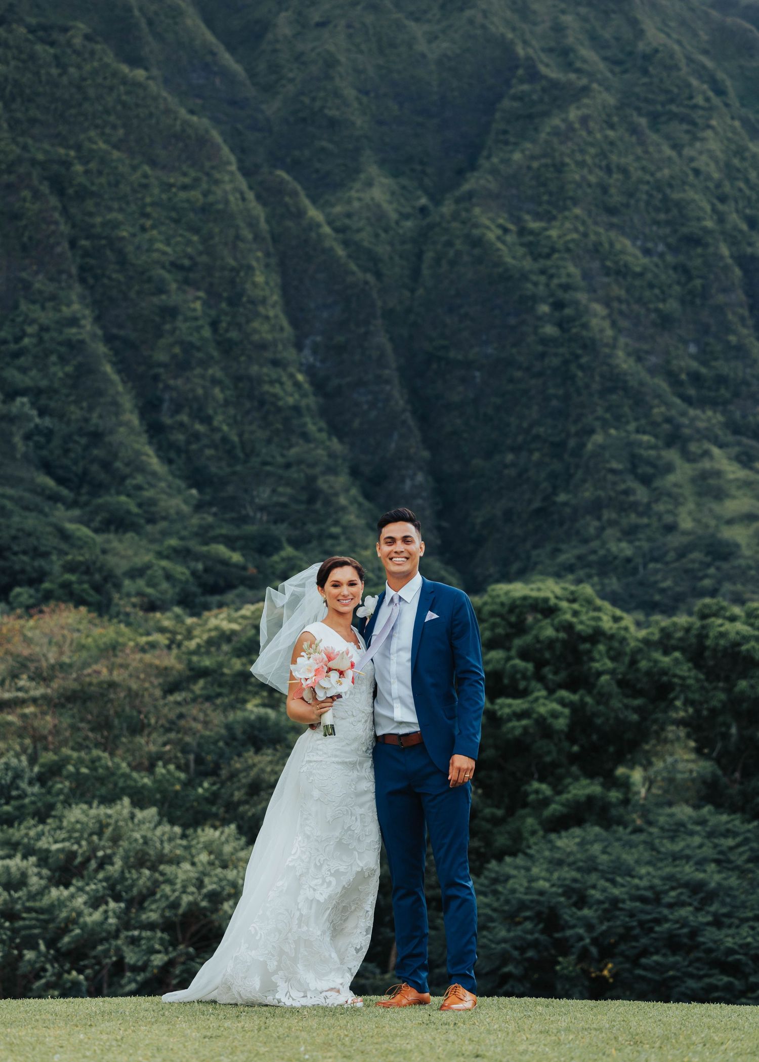 A couple poses for wedding photos against a backdrop of lush Hawaiian mountains in Ko'olau Range.