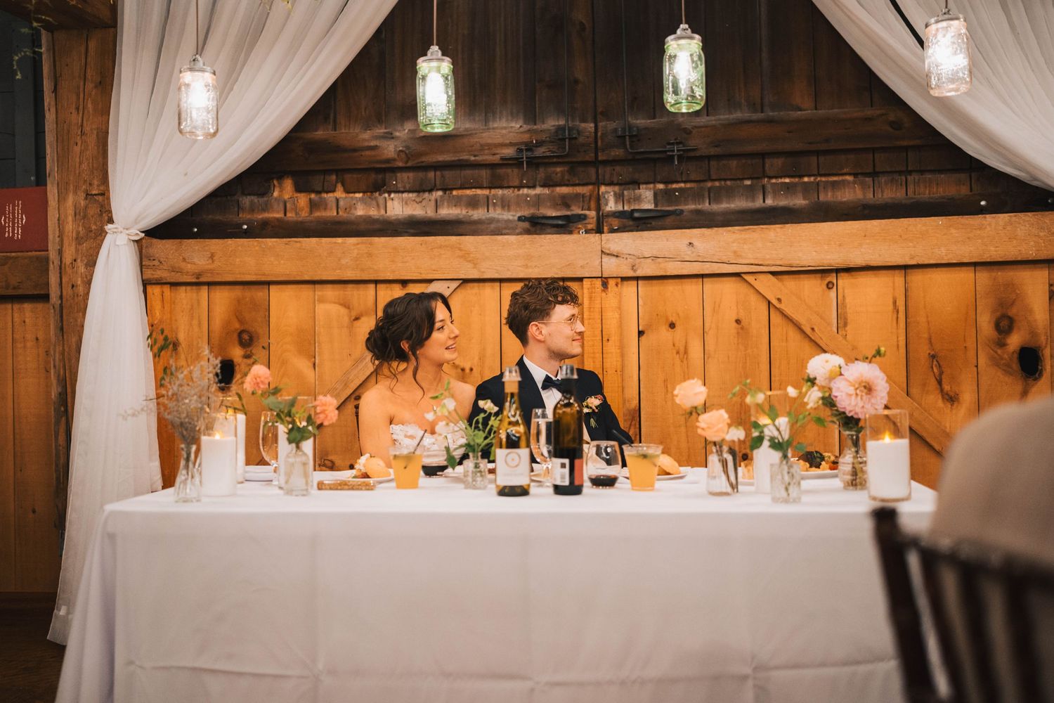 Elegant wedding reception venue with white drapes, hanging lights and rustic wood paneling decor.