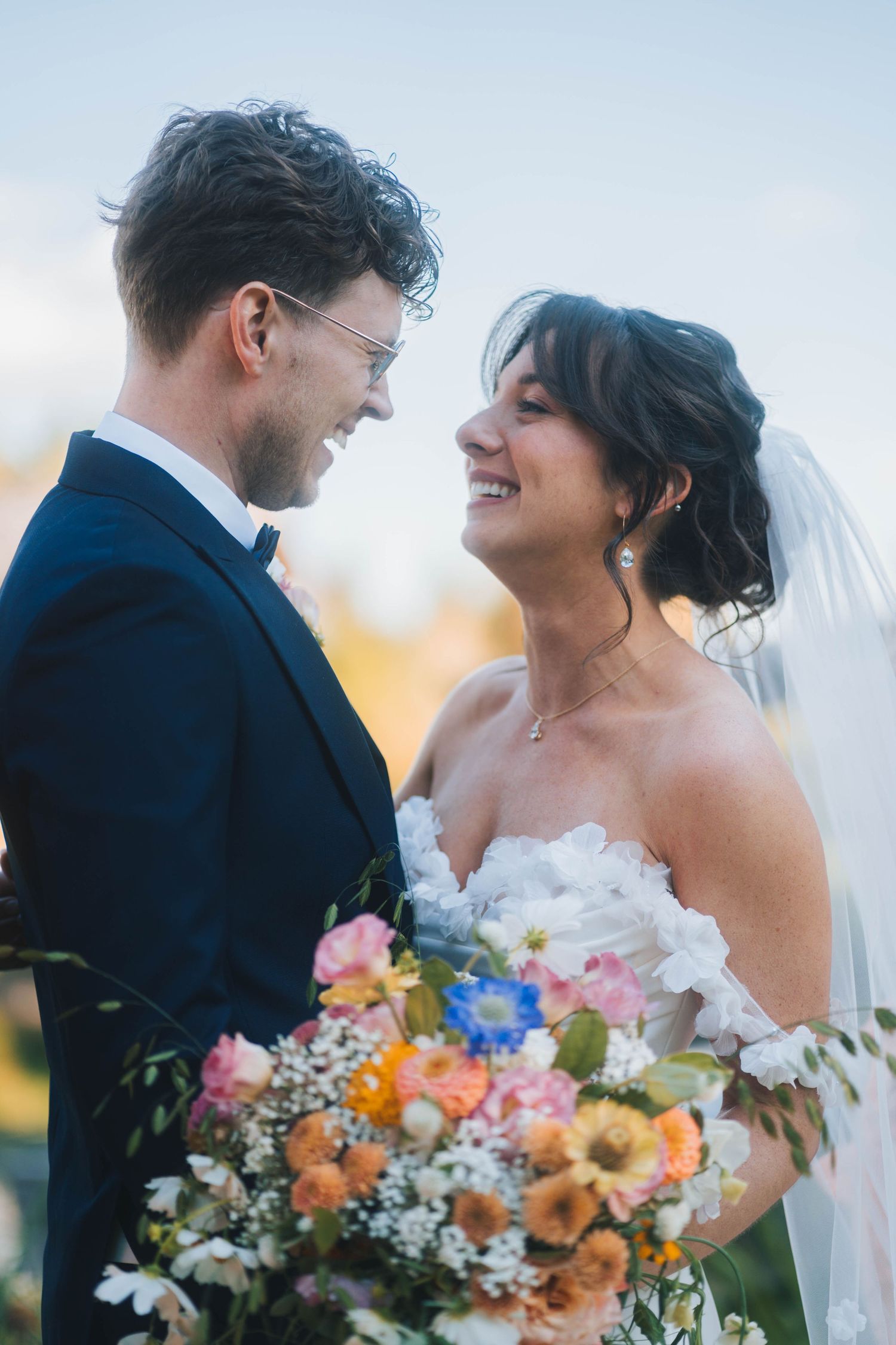 A happy couple shares a joyful moment on their wedding day with a vibrant orange and pink bouquet.
