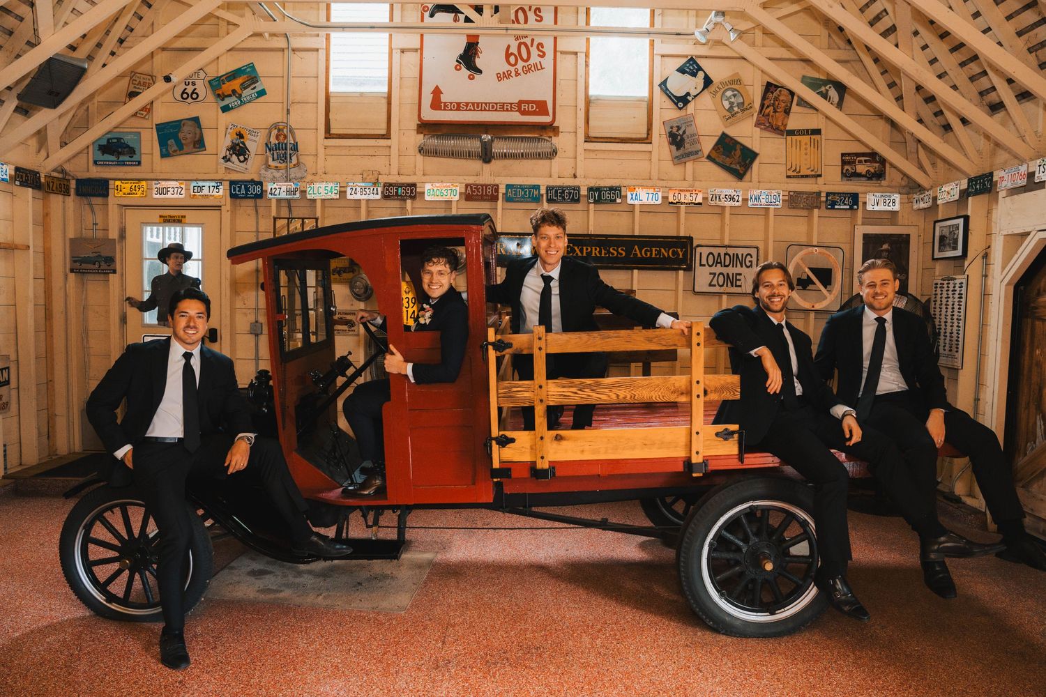 A panoramic view of a vintage car museum interior showing multiple classic automobiles and wooden beamed architecture.