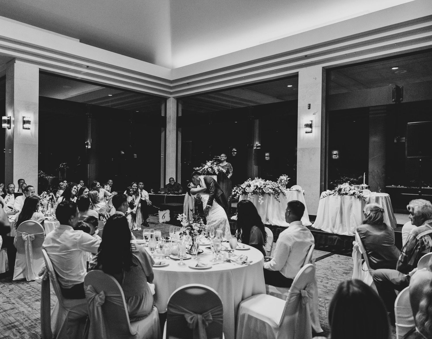 Black and white photo of a formal dining event with guests seated at round tables in an elegant banquet hall.