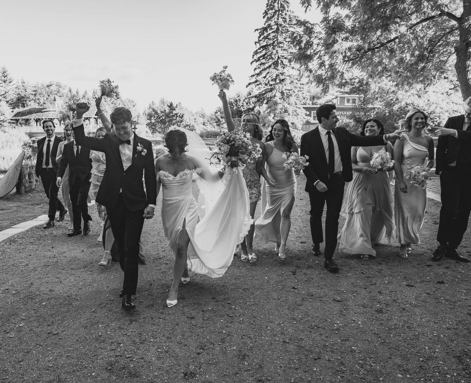 Wedding party walks together in a line across a grassy field during an outdoor celebration in black and white.