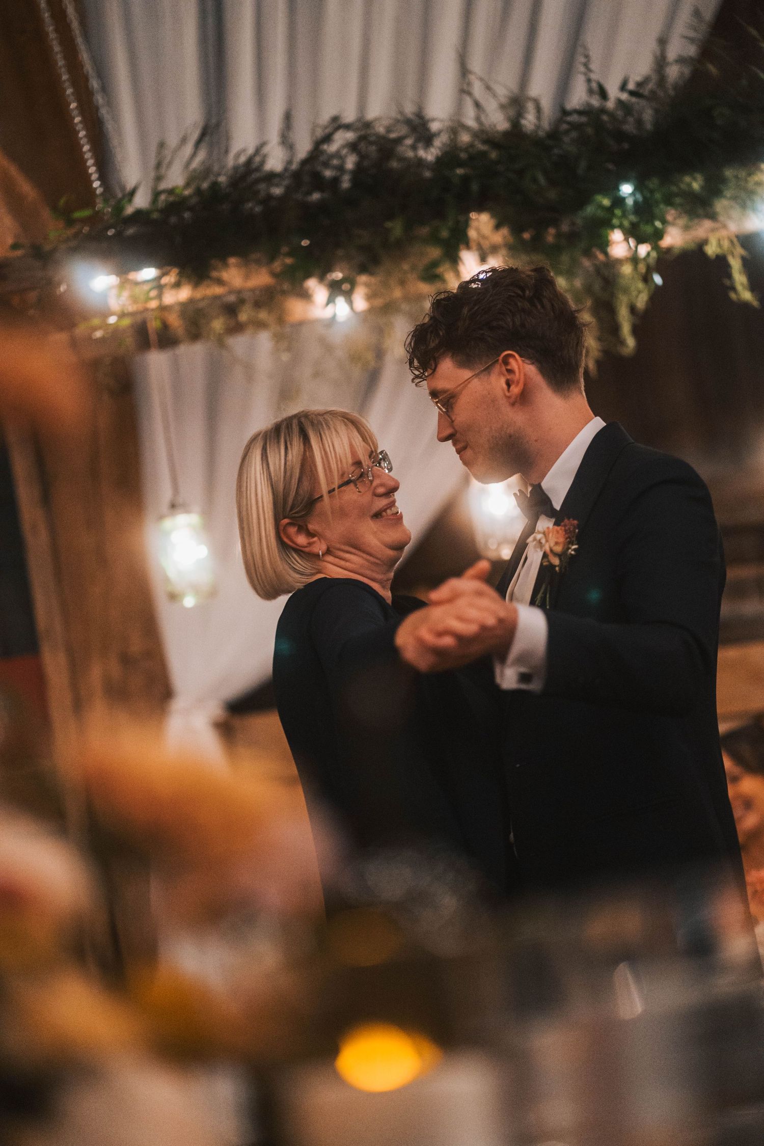 A romantic wedding reception moment captured in warm lighting with a couple dancing intimately in a decorated indoor venue.