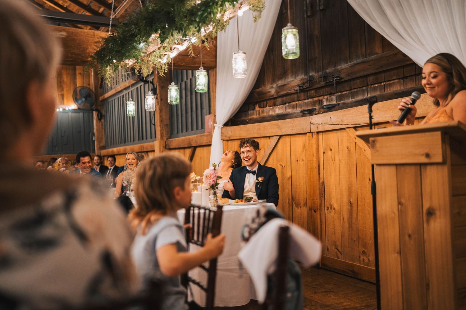 A rustic barn wedding reception venue with warm wooden walls and white drapes creating an intimate atmosphere.