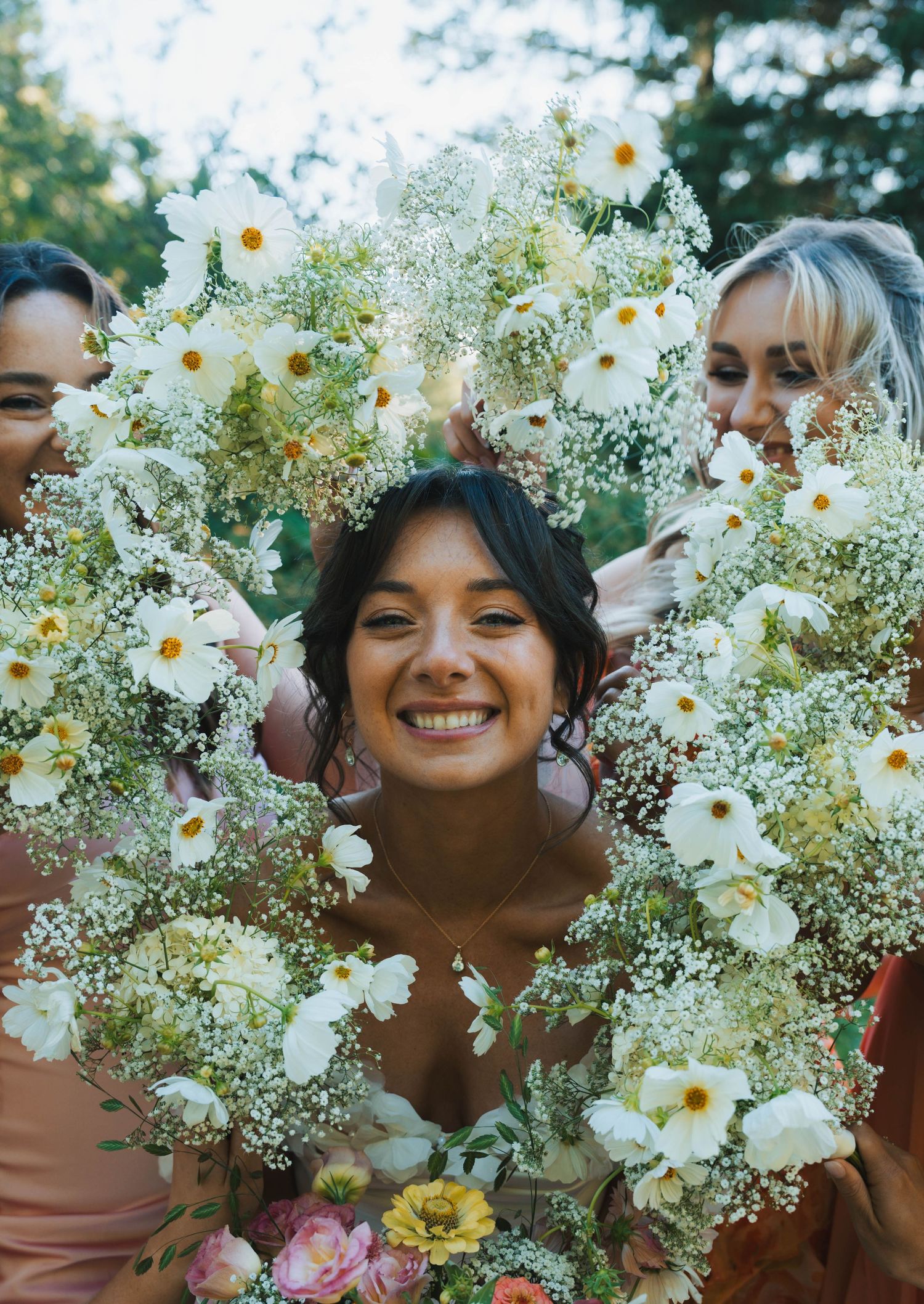 A joyful moment captured through a wreath of white daisies and baby's breath flowers in an outdoor setting.