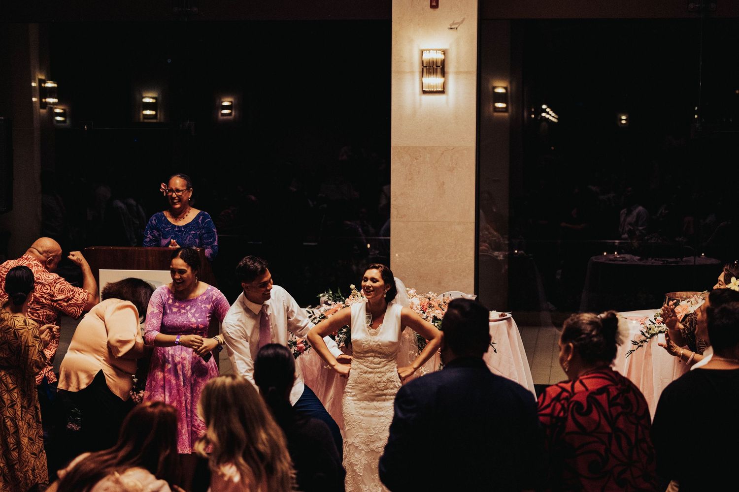 Wedding guests dance and celebrate together during an evening reception in a warmly lit venue.