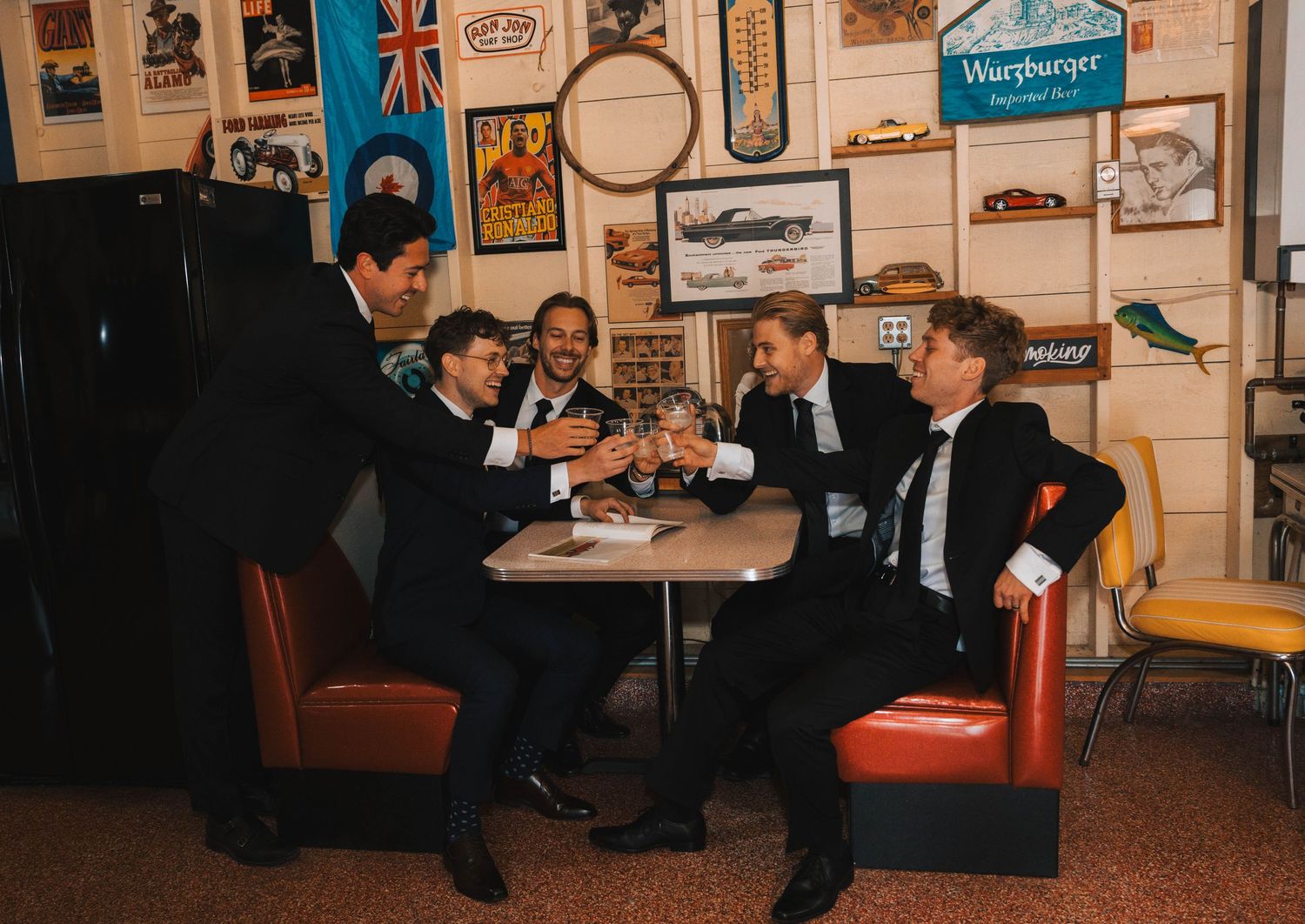 Musicians perform with guitars and instruments in a cozy vintage room decorated with posters and memorabilia on the walls.