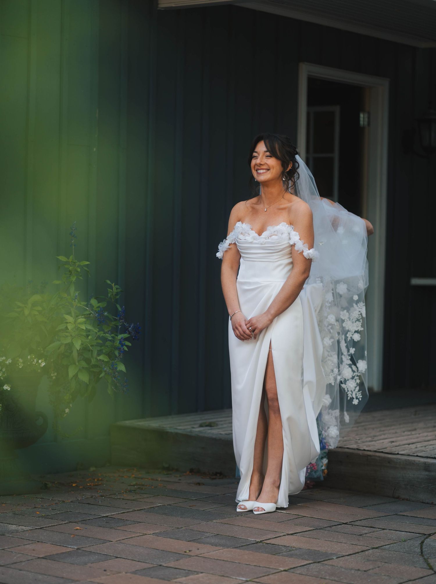 A bride in a white wedding dress poses gracefully on a tiled patio with a veil flowing behind her.